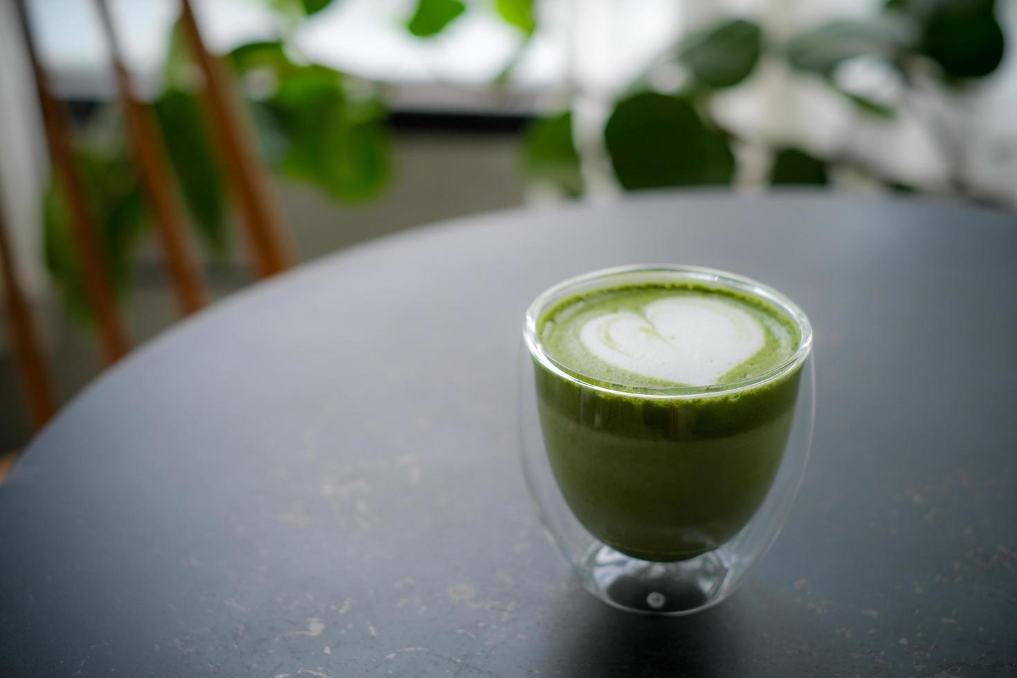 Colse up hot matcha green tea latte art in double walled glass on table in the cafe. photo