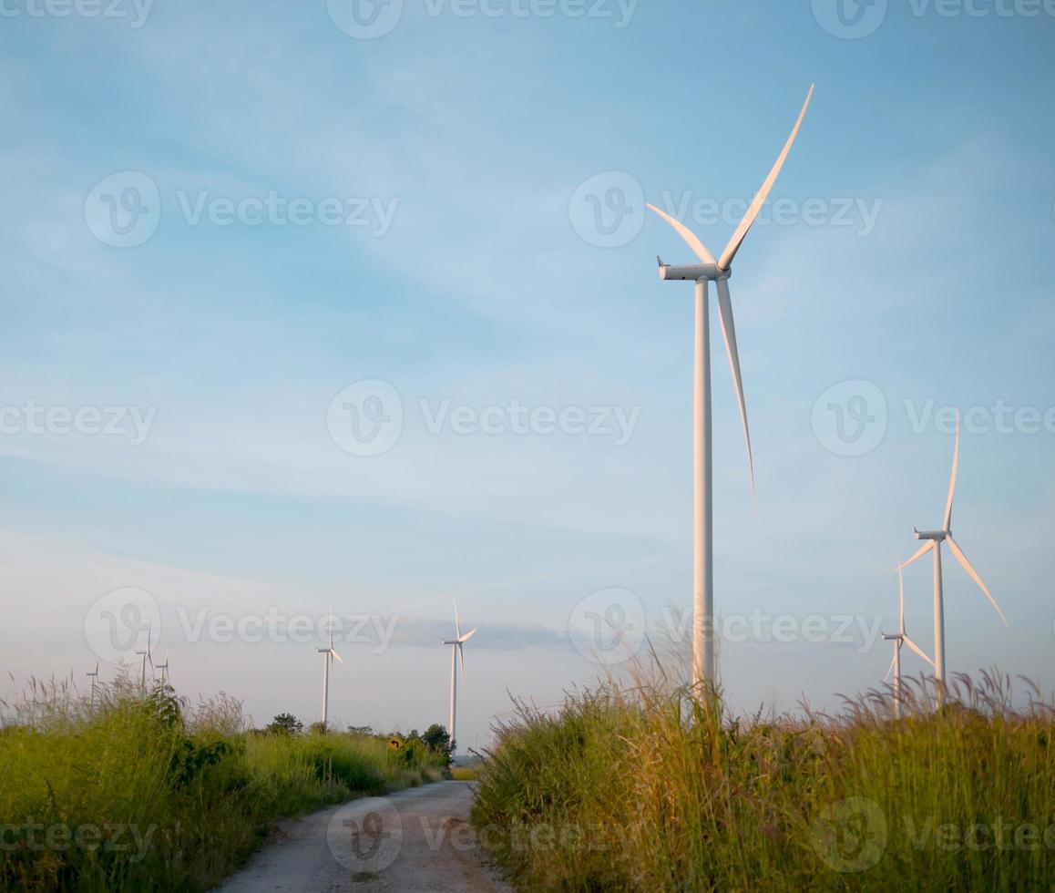 Wind turbine in grass field with Dirt road and blue sky photo
