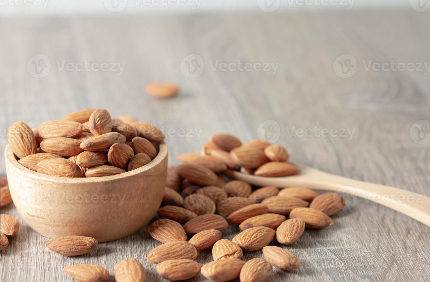 semillas de almendras desbordan un cuenco de madera marrón y el suelo se cae. grupo de almendras en cuchara de madera. foto