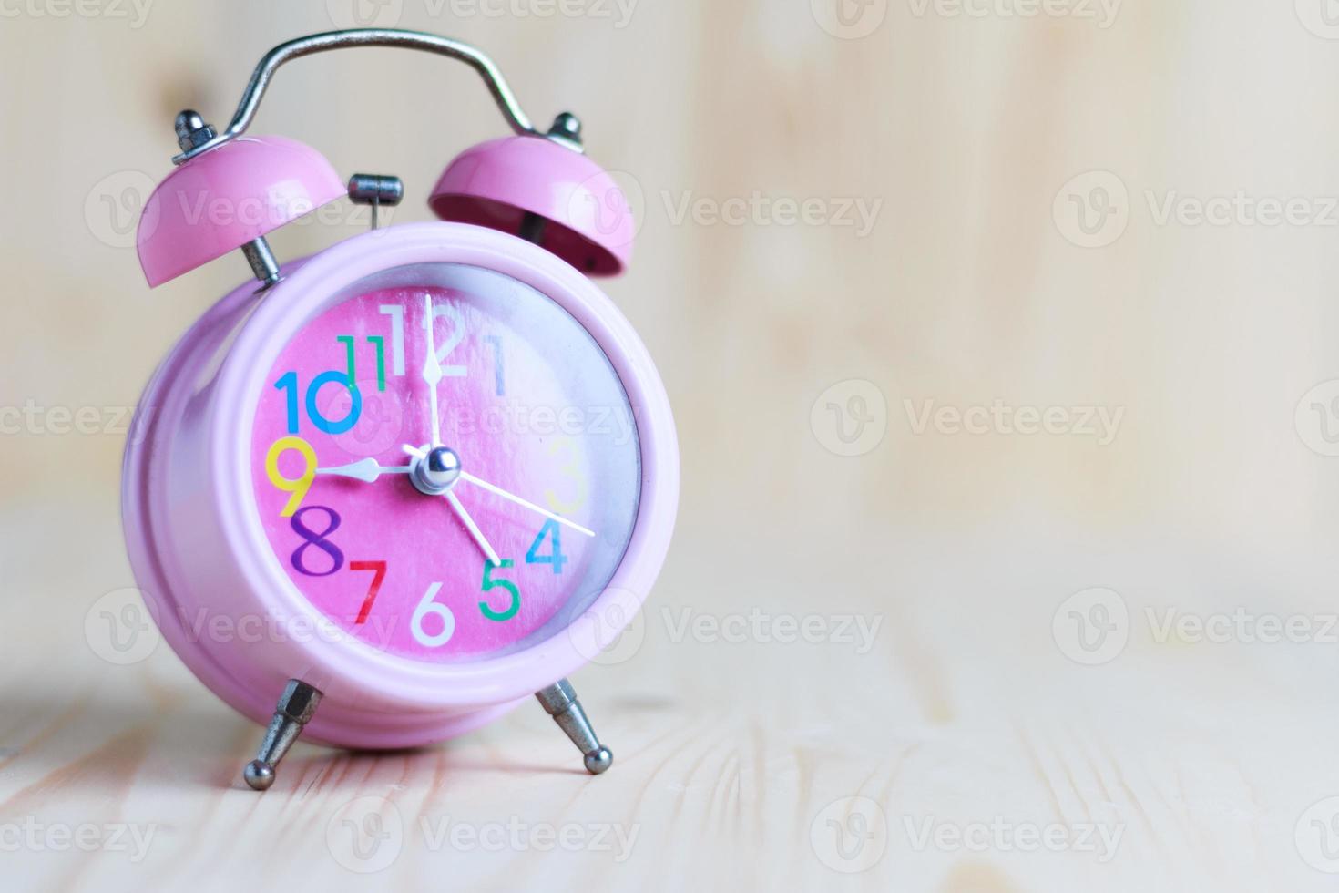 The Pink alarm clock place on the wooden table and wood background photo