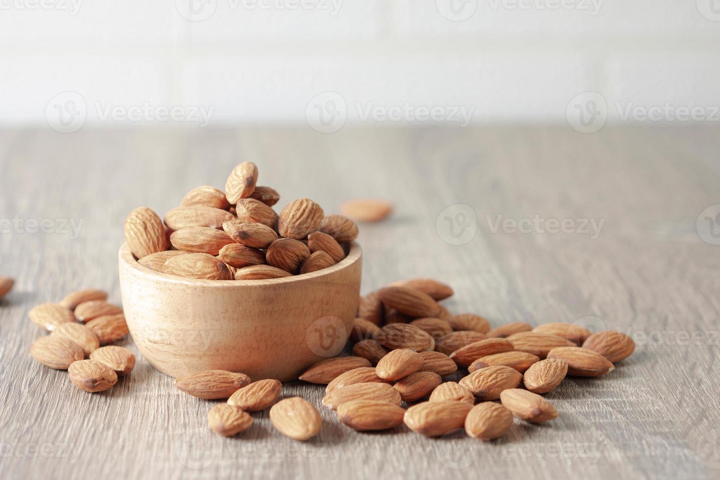 Almond seeds overflow a brown wooden bowl and the floor fell photo