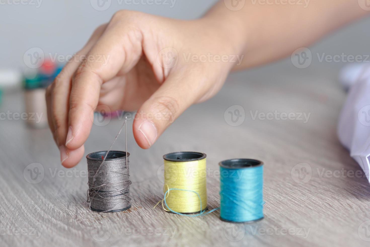 The woman's hand was about to pick up the thread that was placed on the table to sew photo