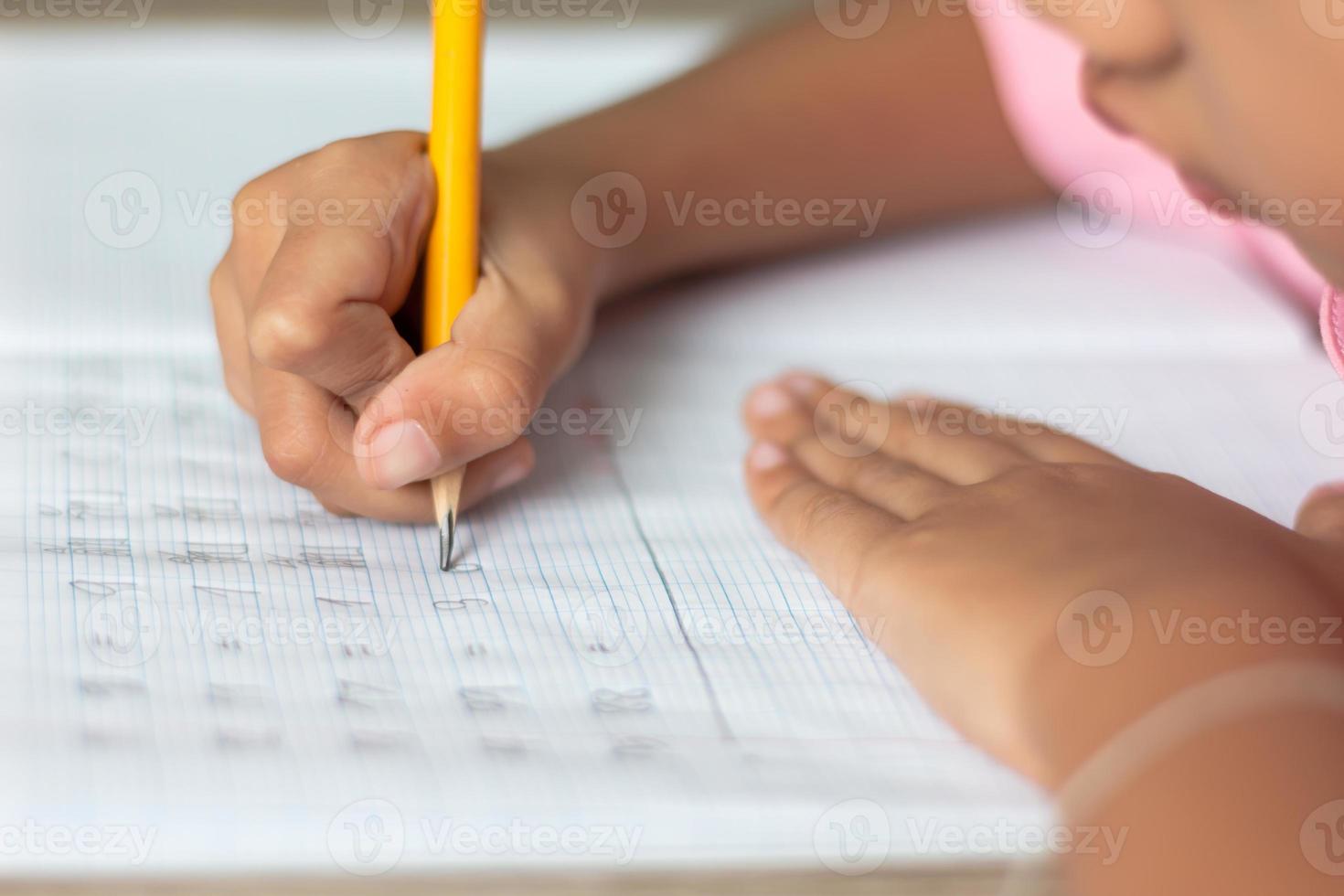 Hand is holding a yellow pencil and writing in a notebook photo