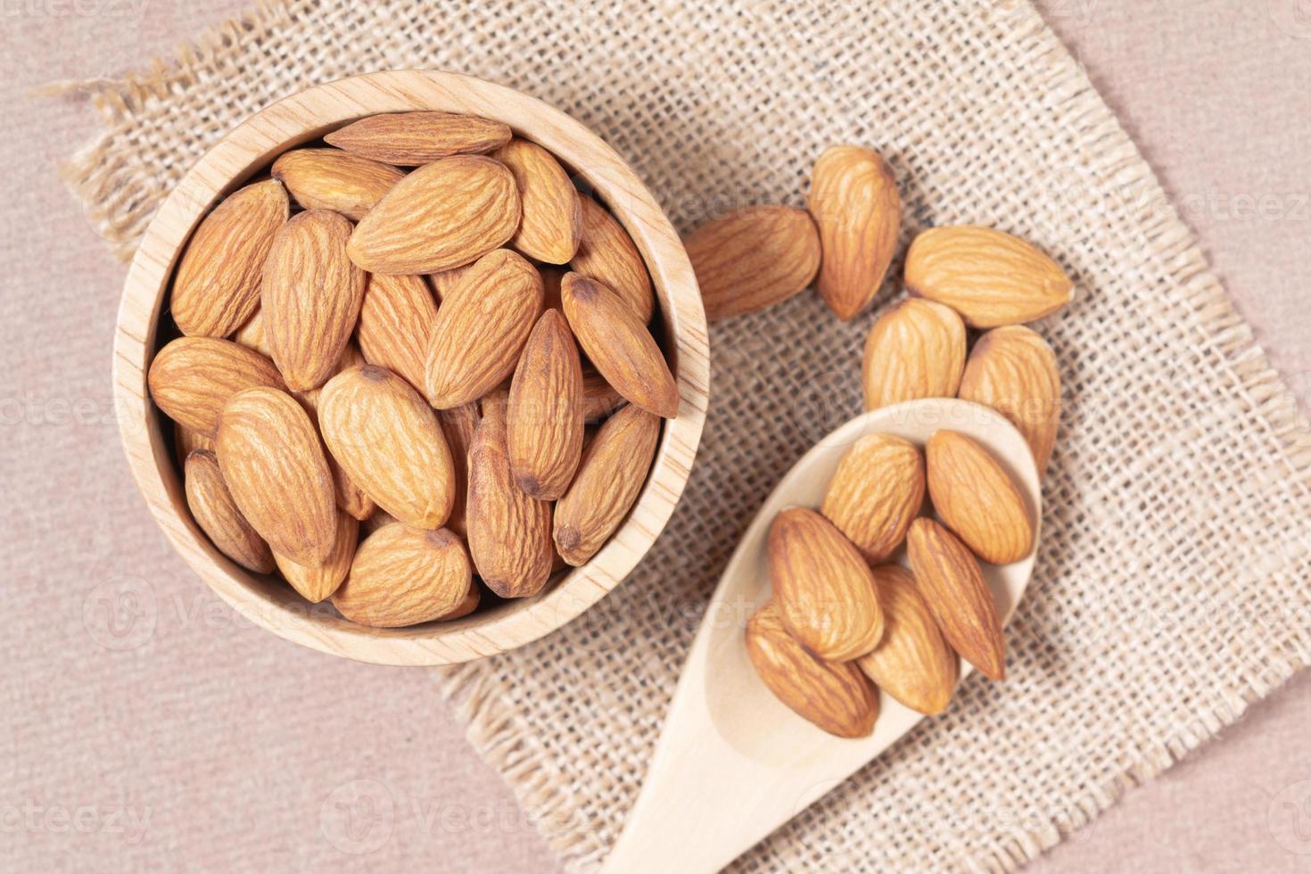 Almond seeds in a cup and spoon are placed on a woven sack and wood table photo