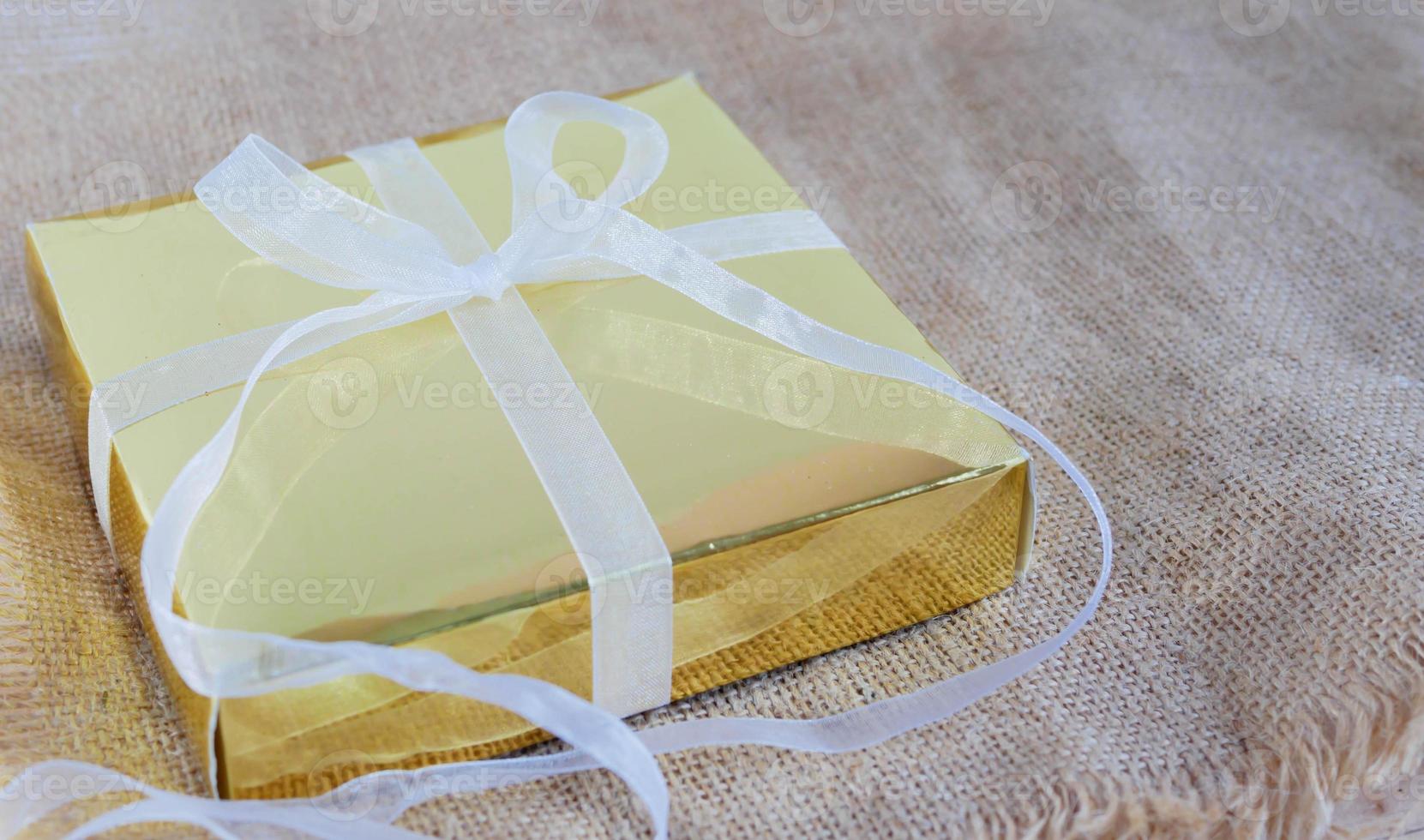 Gold gift box with white ribbon on the brown sack photo