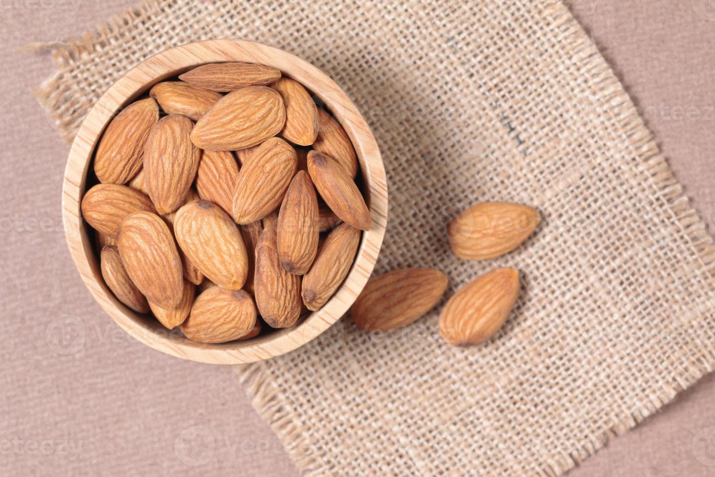 Almond seeds in a cup are placed on a woven sack and wood table photo