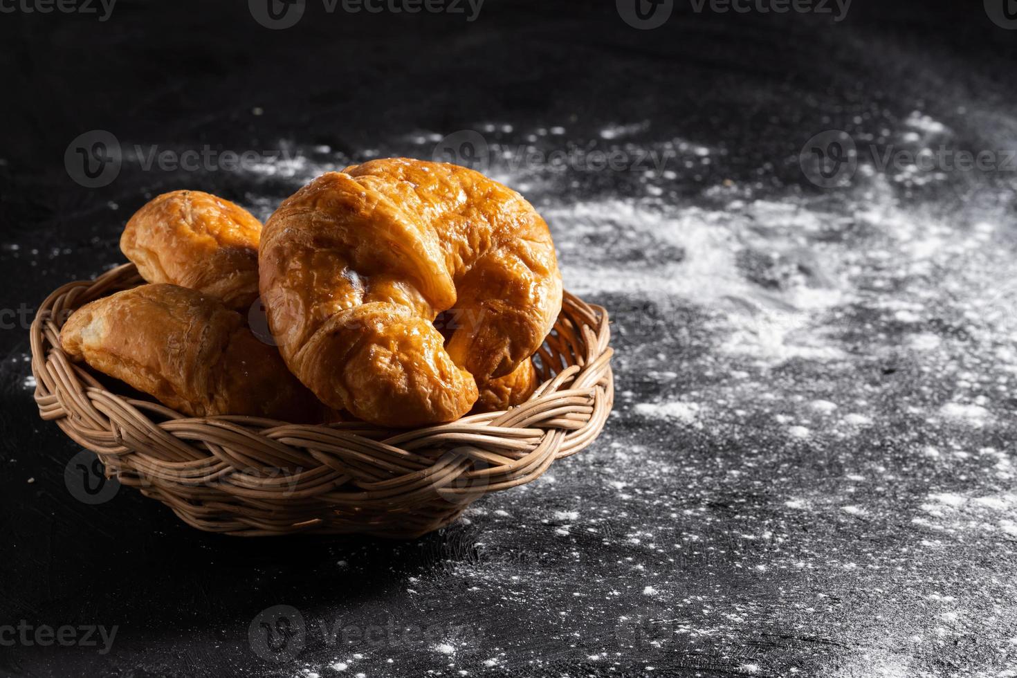 Croissants in a wicker basket placed on a black floor photo