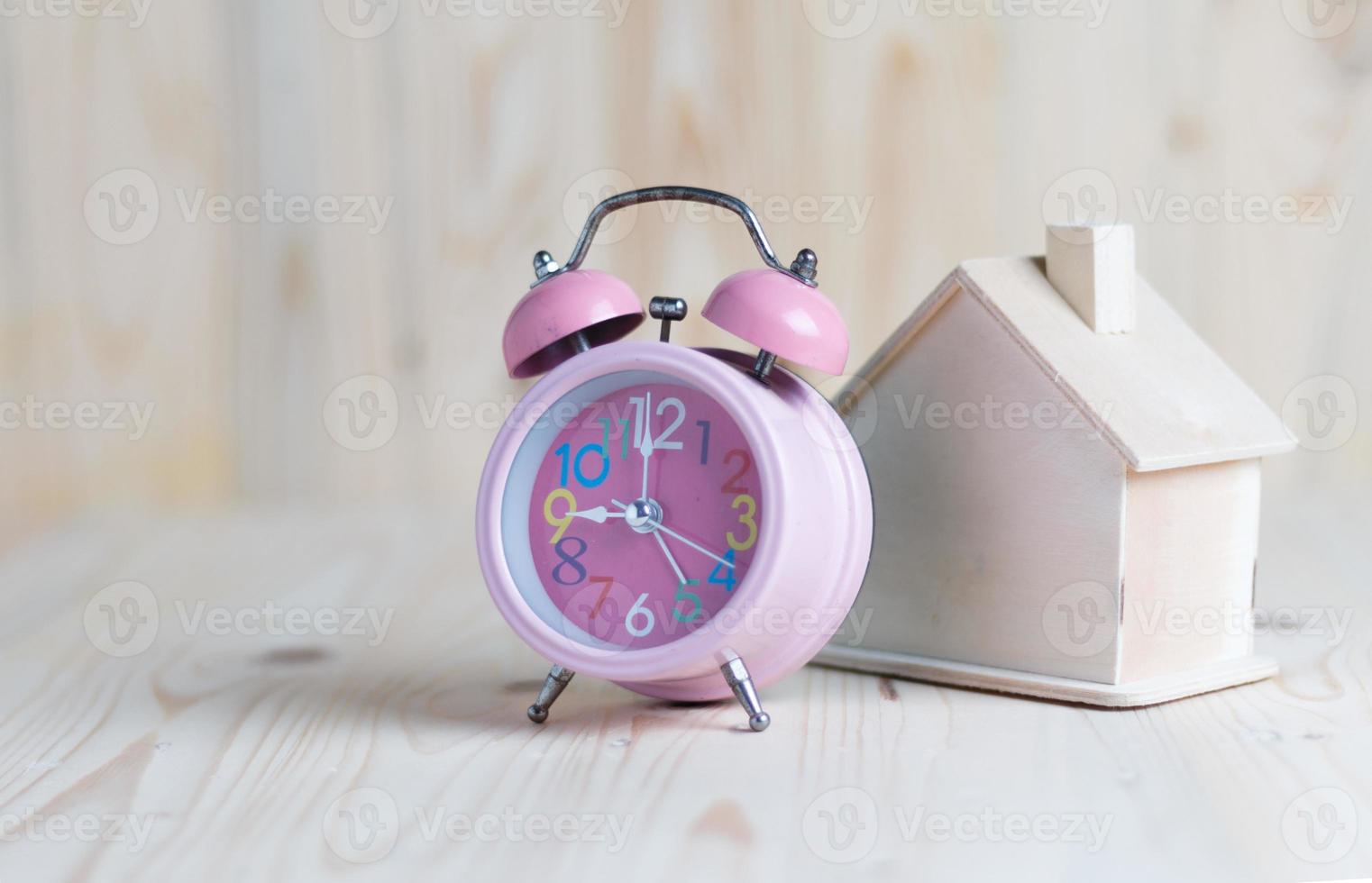 Pink alarm clock and a house place on the wooden table and wood background photo