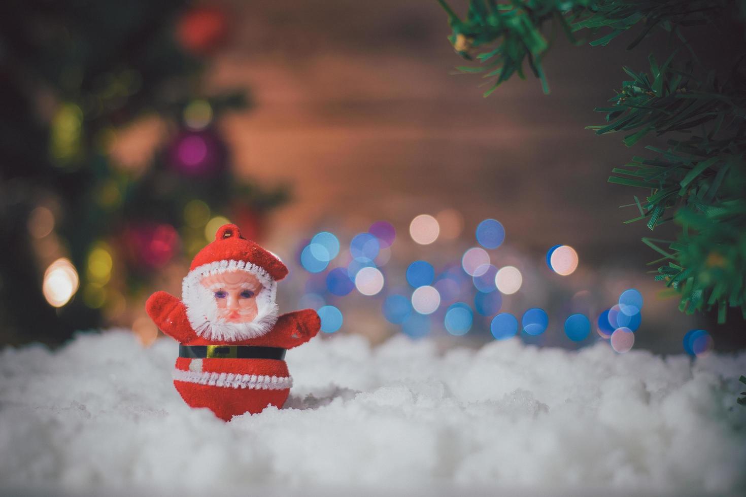 Santa Claus doll  placed on the snow and the Christmas tree background with bokeh and wood. photo