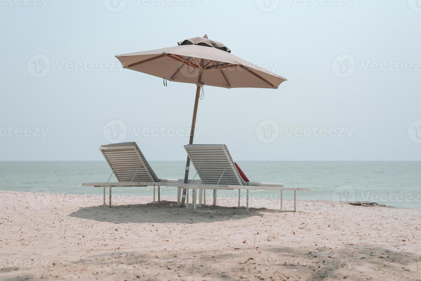 Two sun-beds and umbrella on tropical beach - vacation time photo