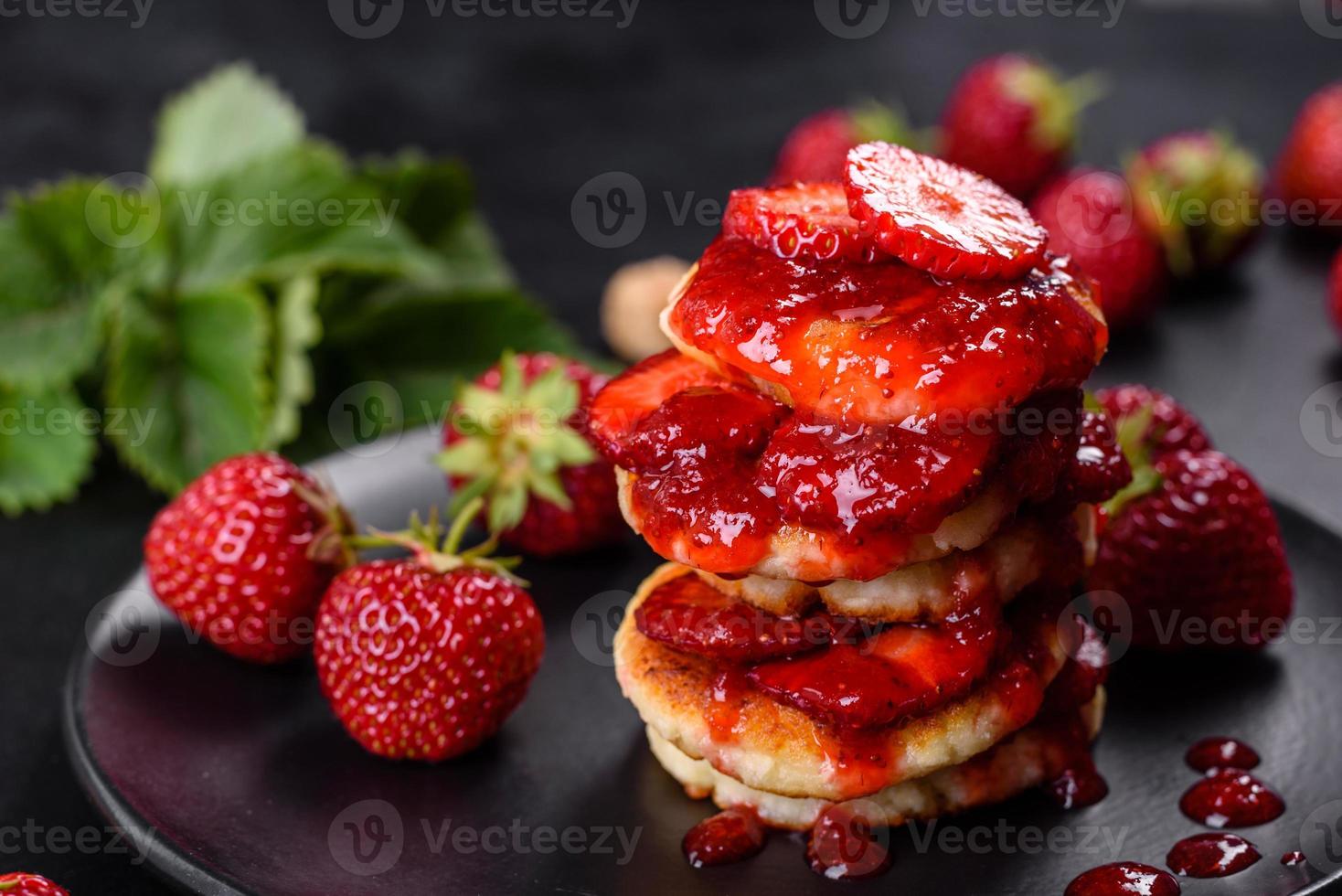 Cottage cheese pancakes with sliced strawberries and strawberry jam on a plate on a concrete background photo