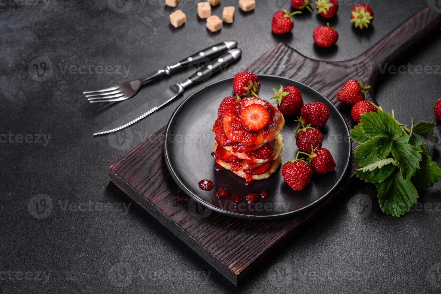 Cottage cheese pancakes with sliced strawberries and strawberry jam on a plate on a concrete background photo