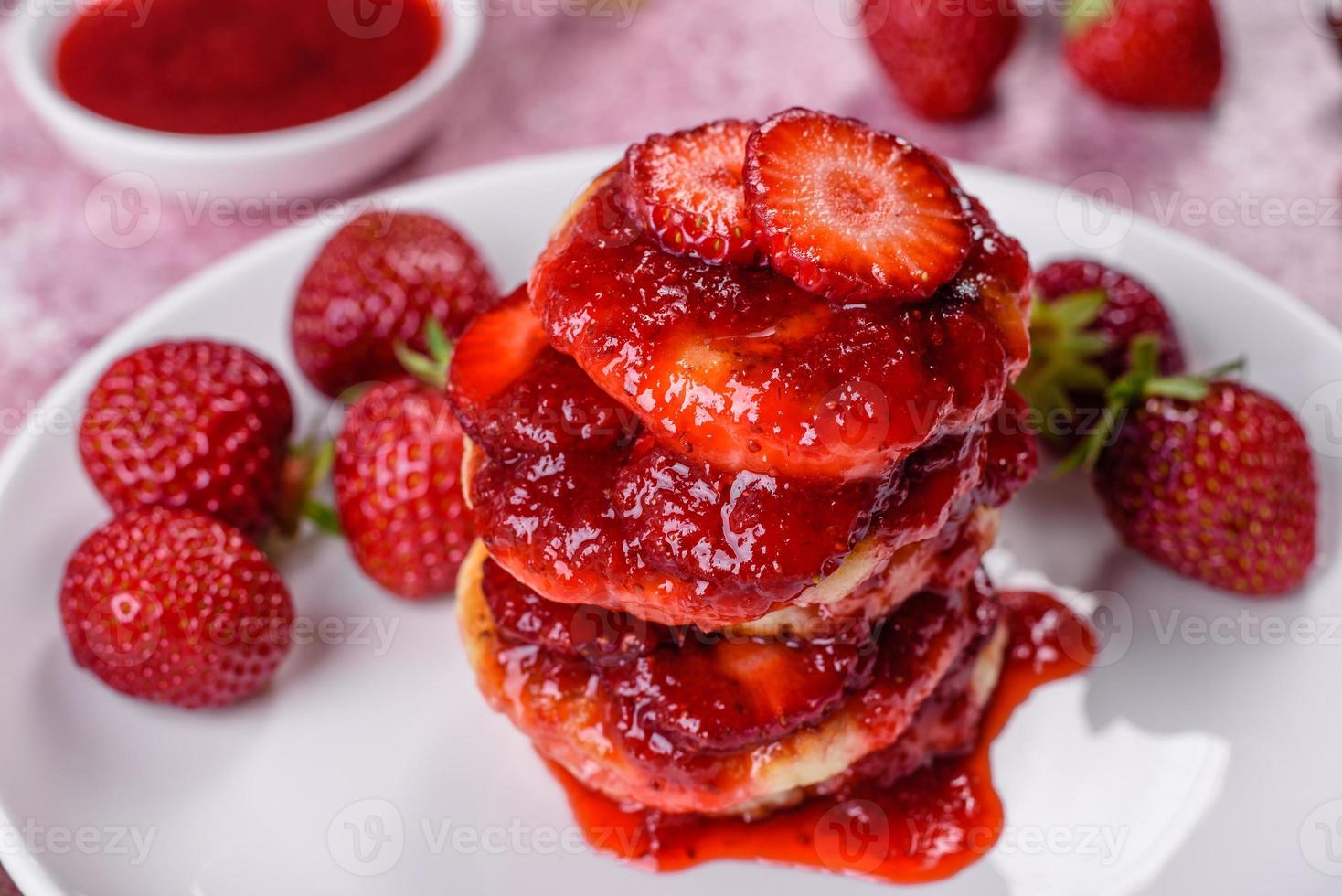 tortitas de requesón con fresas en rodajas y mermelada de fresa en un plato sobre un fondo de hormigón foto
