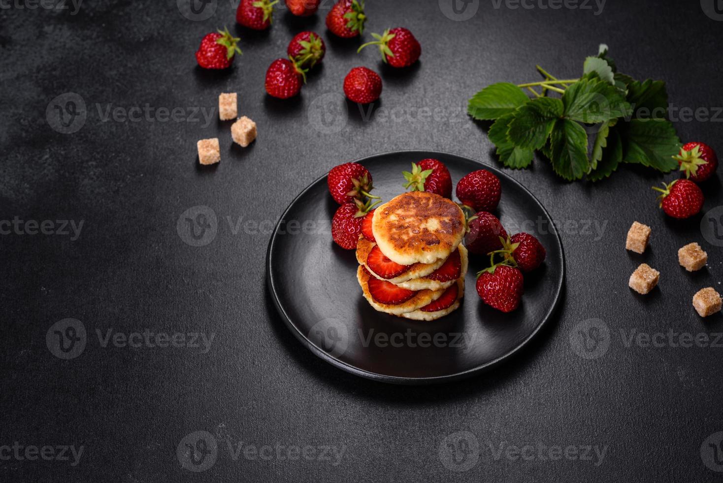 Cottage cheese pancakes with sliced strawberries and strawberry jam on a plate on a concrete background photo