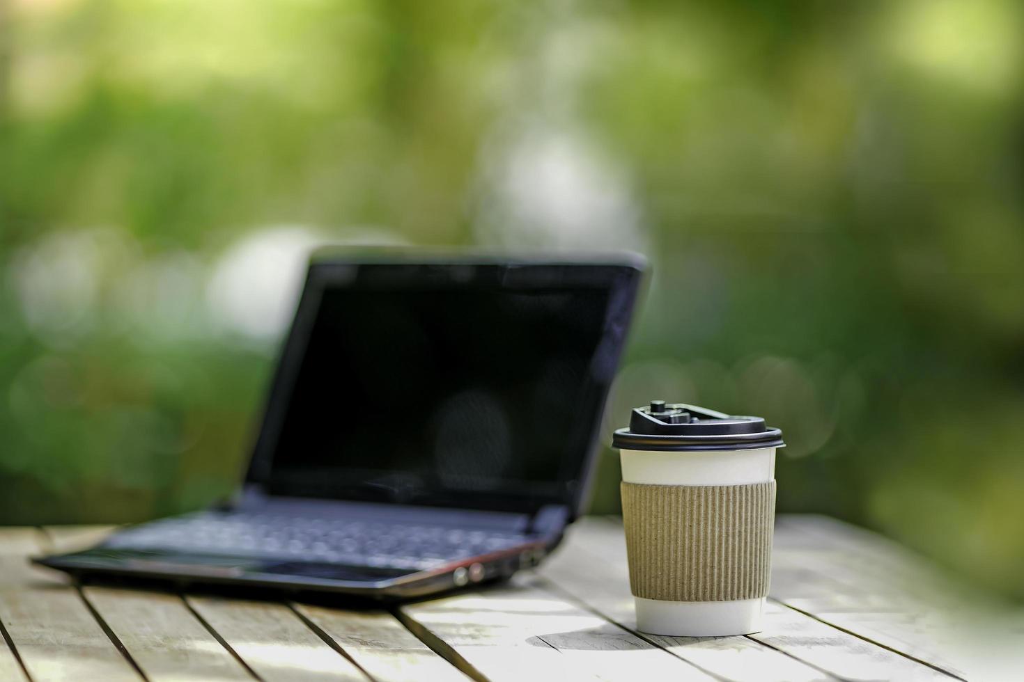 coffee cup paper with a Computer laptop in green nature background. Work remotely or from home. soft focus.shallow focus effect. photo