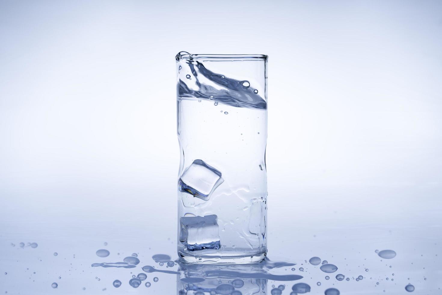 el cubo de hielo cayó en el vaso de agua. agua salpicada del cristal transparente. concepto fresco foto