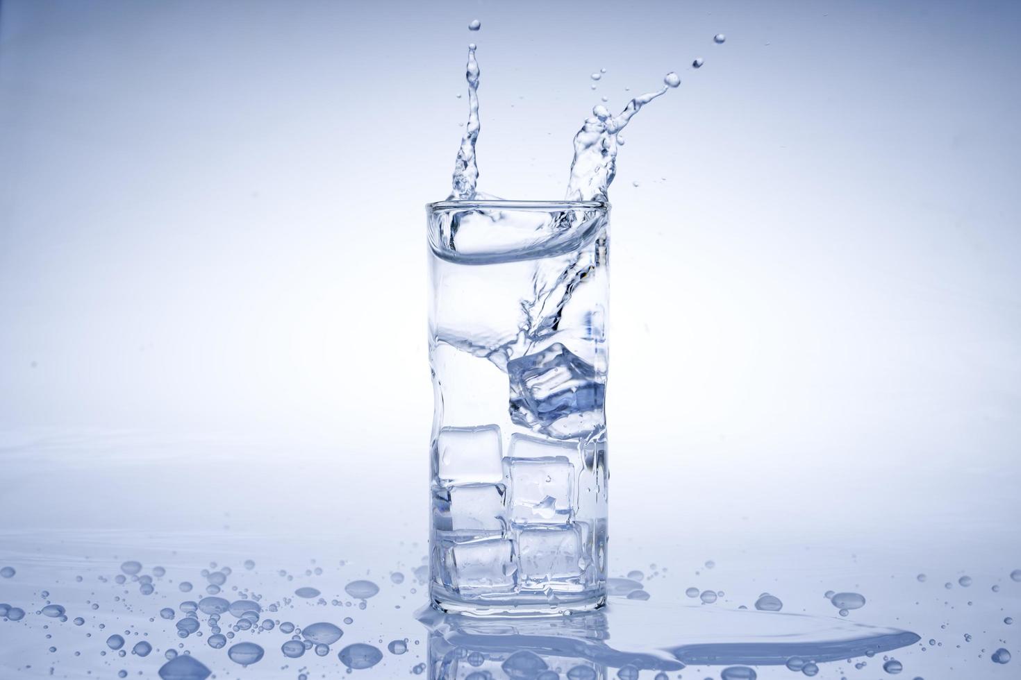 el cubo de hielo cayó en el vaso de agua. agua salpicada del cristal transparente. concepto fresco foto