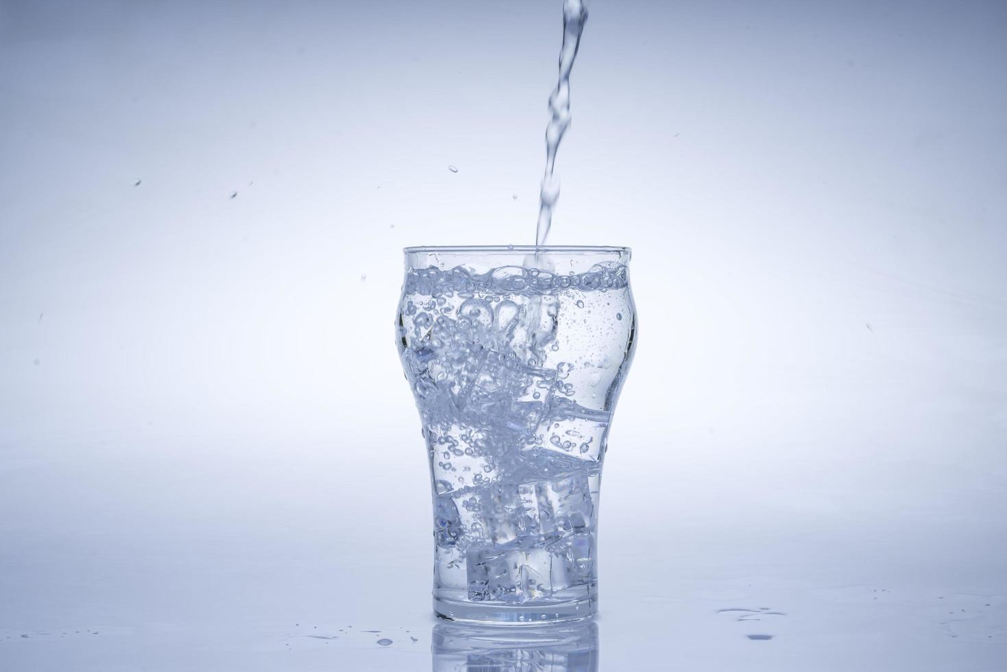 cubo de hielo cayó en el vaso de agua. agua salpicada del cristal transparente. concepto fresco foto