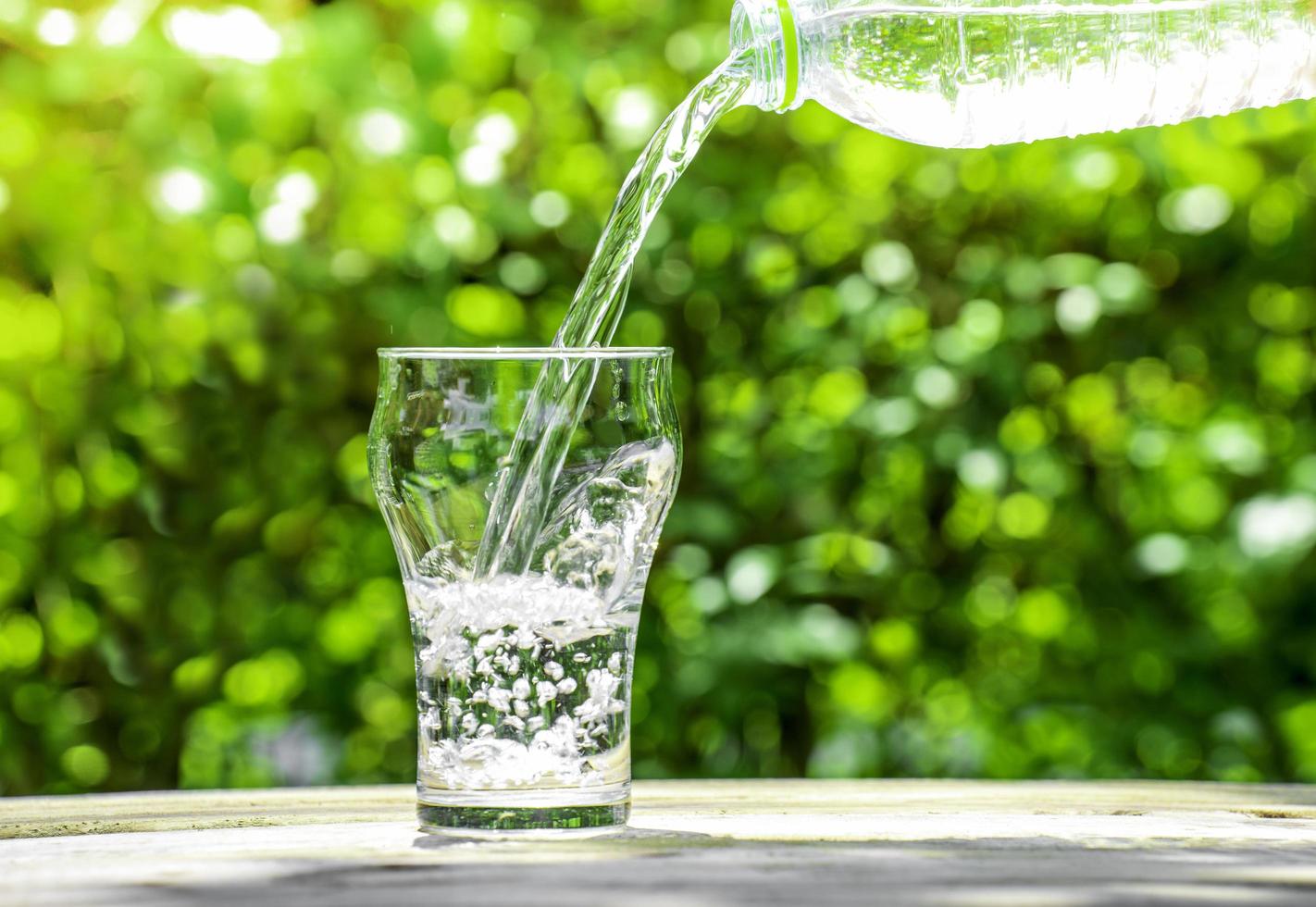 Pour water from a plastic bottle into a glass. The background of the plants in the garden. soft focus. photo