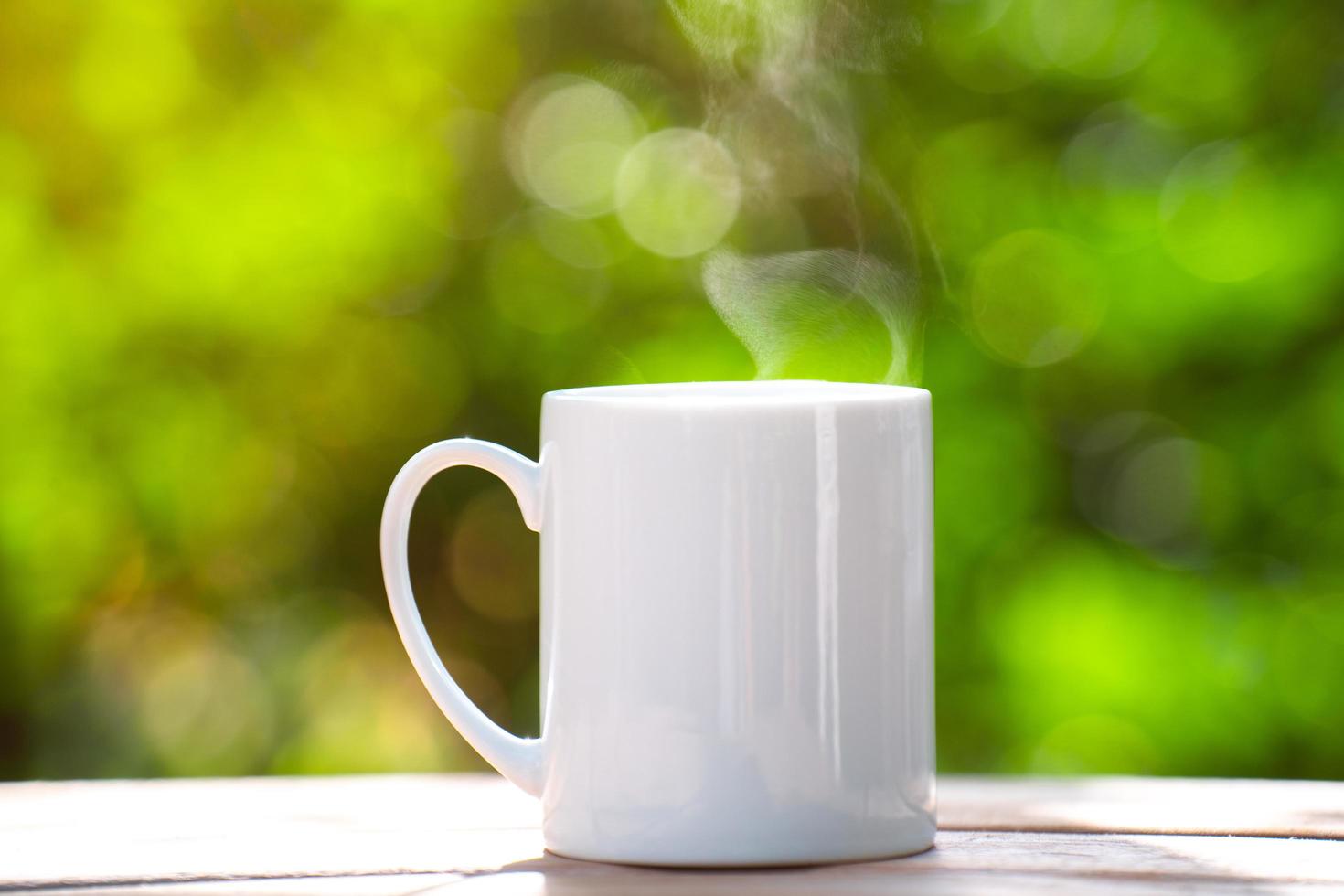 taza de café de cerámica blanca en el suelo de madera, fondo de bokeh de árbol verde. enfoque suave efecto de enfoque superficial. foto