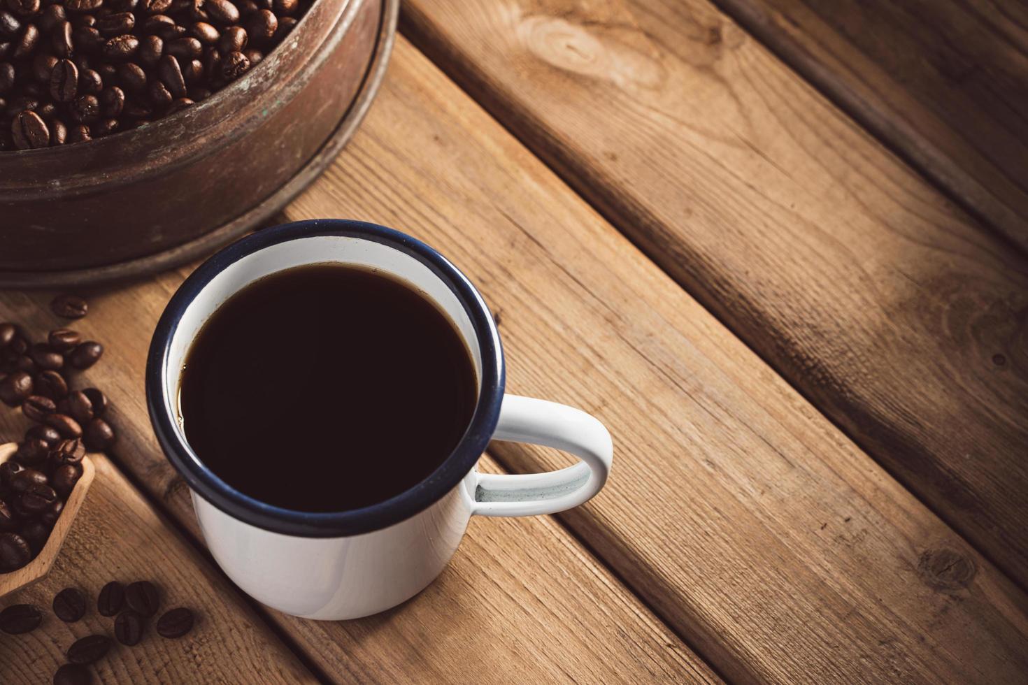 white enamel coffee mug and Dark Coffee beans on the old wooden floor. soft focus.shallow focus effect. photo