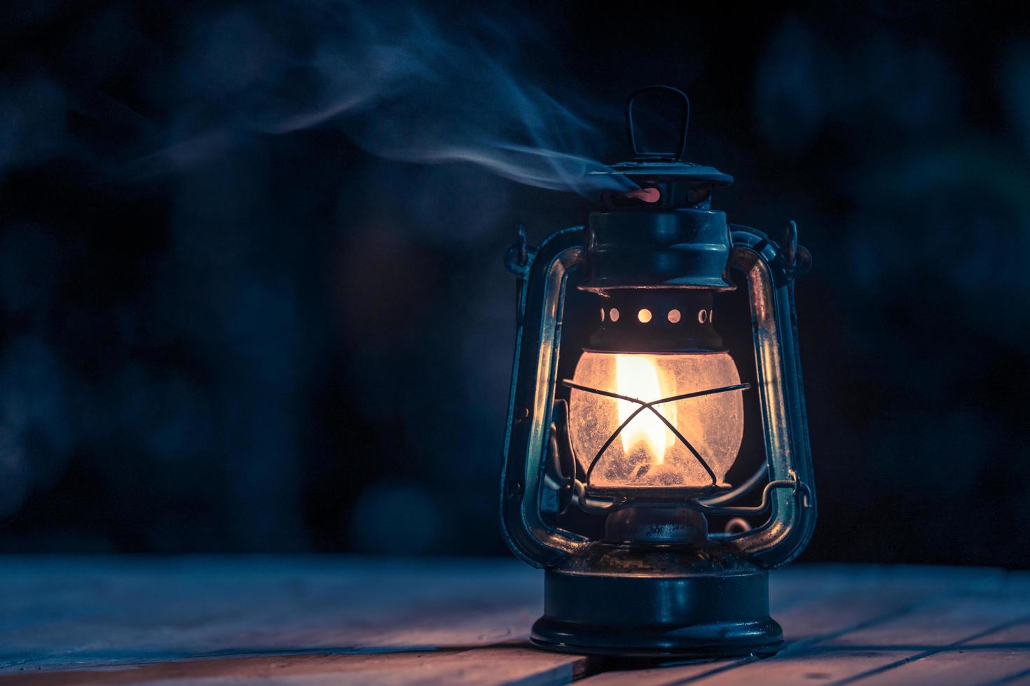 lámpara de queroseno antigua con luces en el suelo de madera en el césped por la noche foto