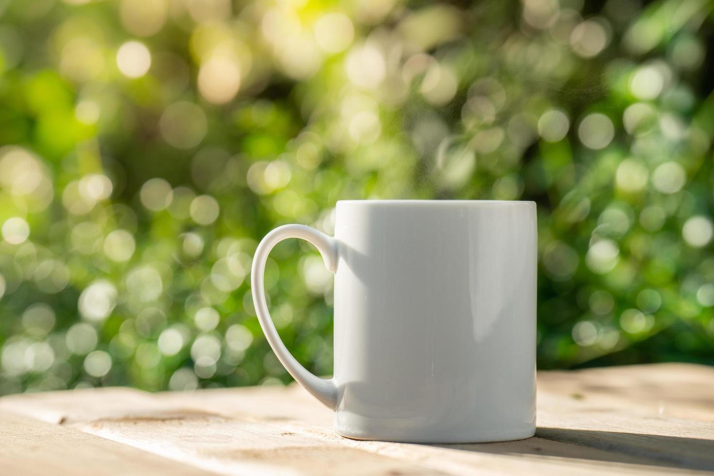 white ceramic coffee mug On the wooden floor, green tree bokeh background. soft focus.shallow focus effect. photo