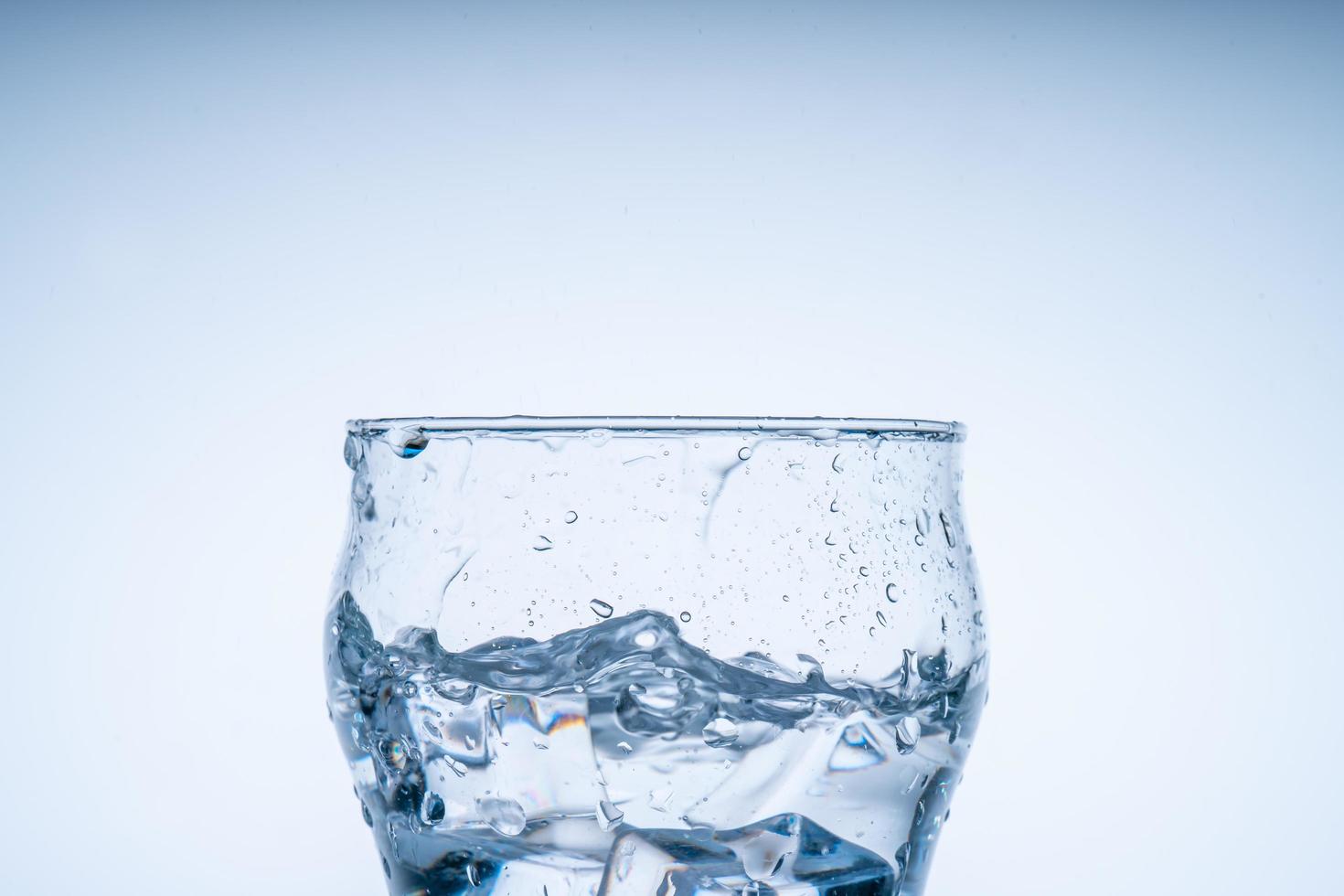 cubo de hielo cayó en el vaso de agua. agua salpicada del cristal transparente. concepto fresco foto