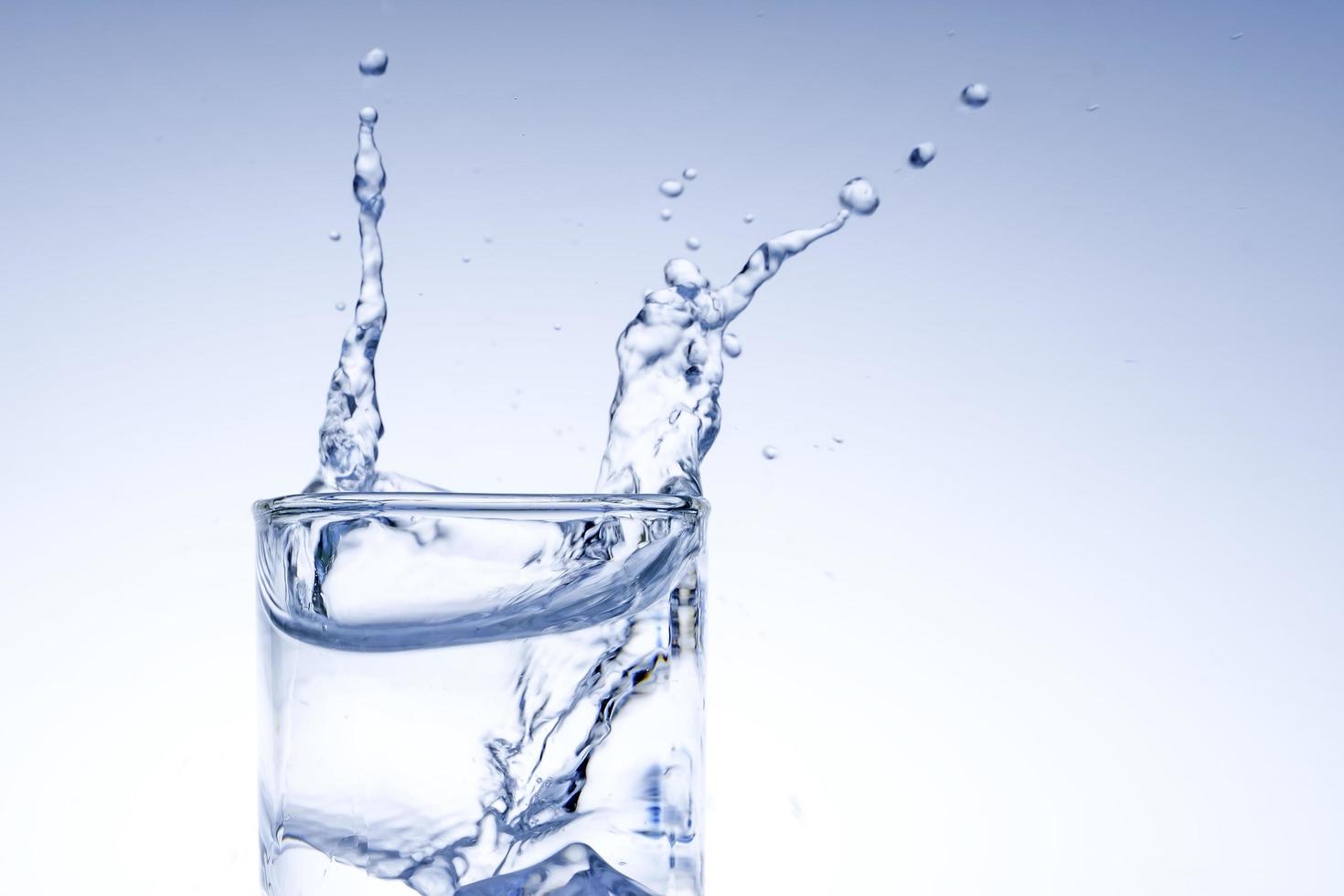 el cubo de hielo cayó en el vaso de agua. agua salpicada del cristal transparente. concepto fresco foto