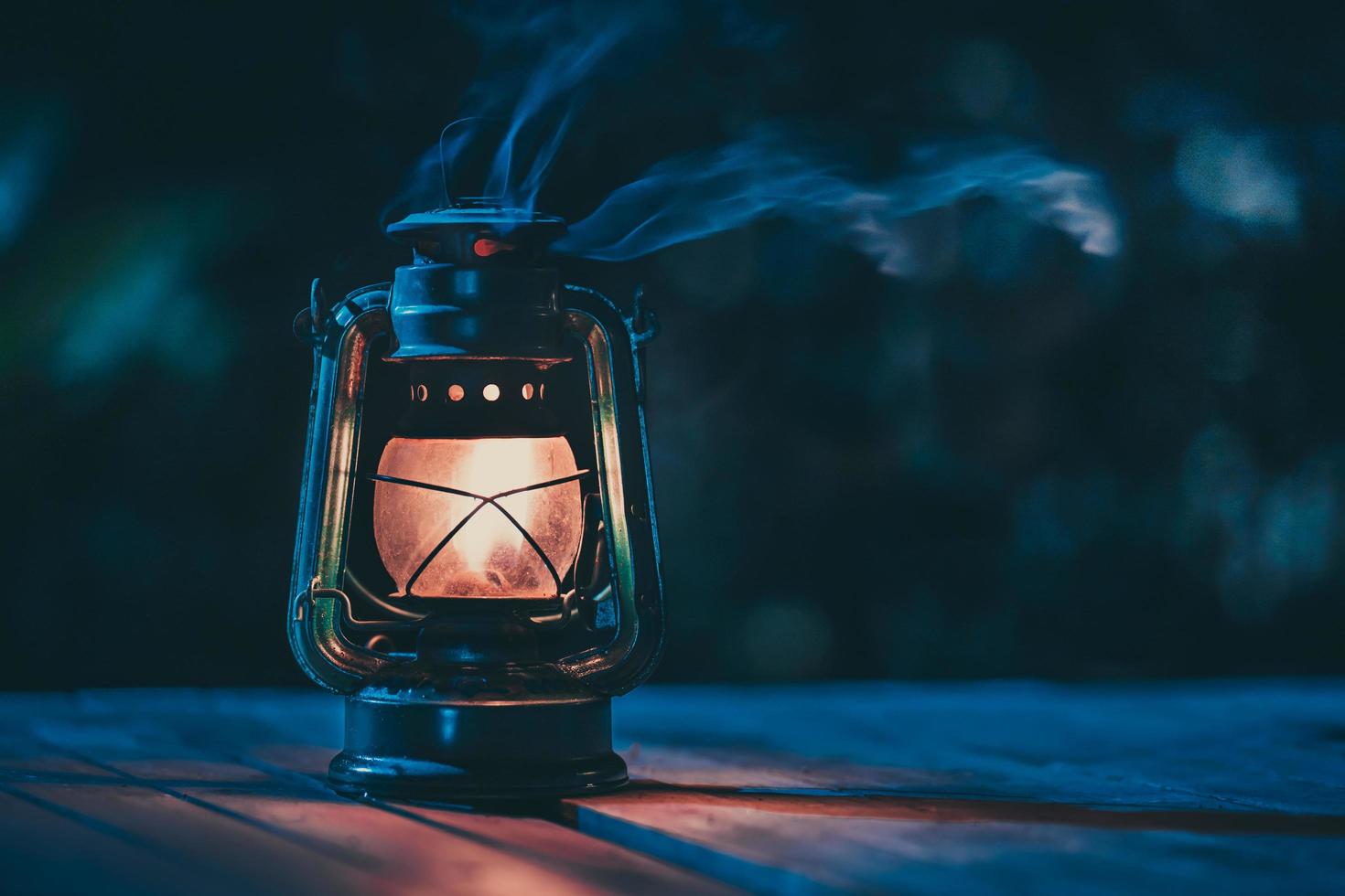 lámpara de queroseno antigua con luces en el suelo de madera en el césped por la noche foto