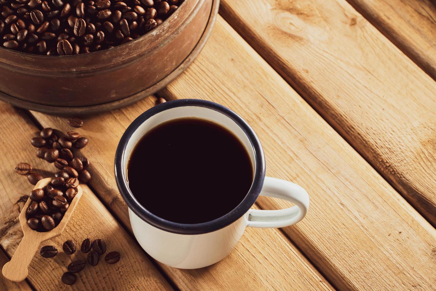 white enamel coffee mug and Dark Coffee beans on the old wooden floor. soft focus.shallow focus effect. photo