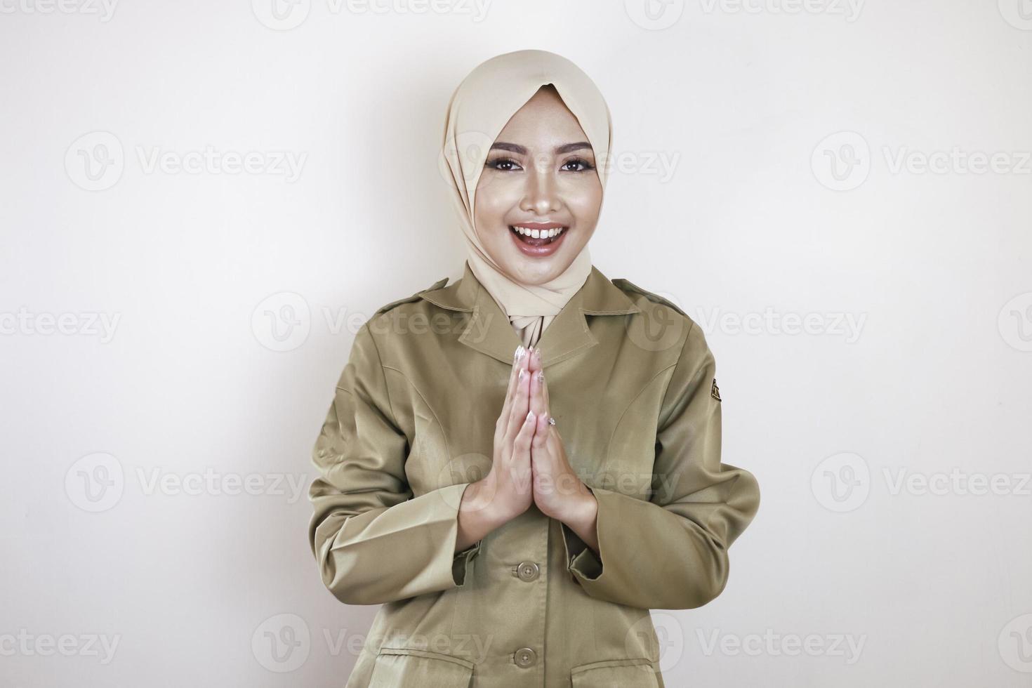 Moslem civil worker wearing brown uniform and hijab greeting with a hand gesture and smiling at the camera photo