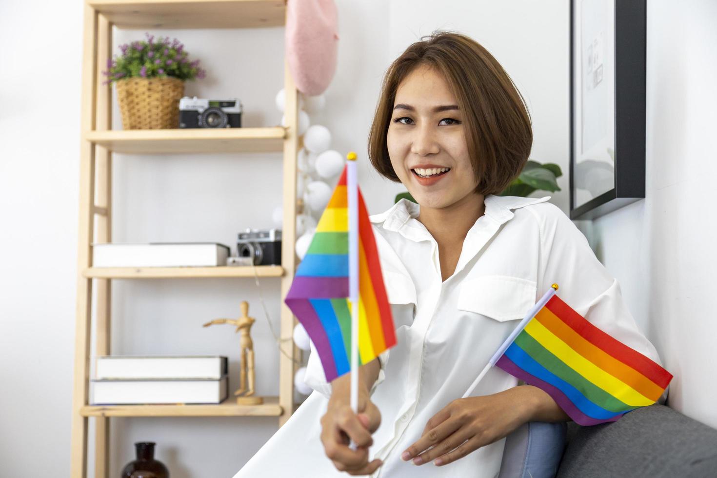 Asian girl holding LGBTQ rainbow flag in her bed room for coming out of the closet and pride month celebration to promote sexual diversity and equality in homosexual orientation concept photo