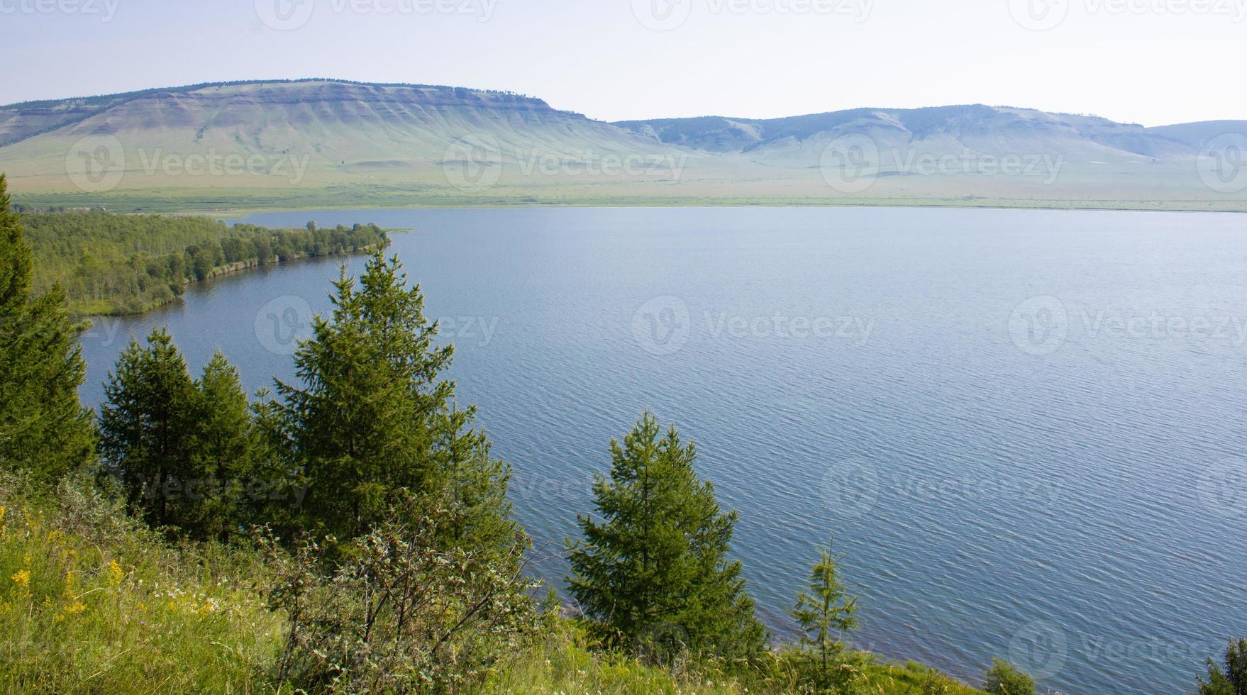 A large lake among trees and mountains on a summer day. Ripples on the surface of the water. photo