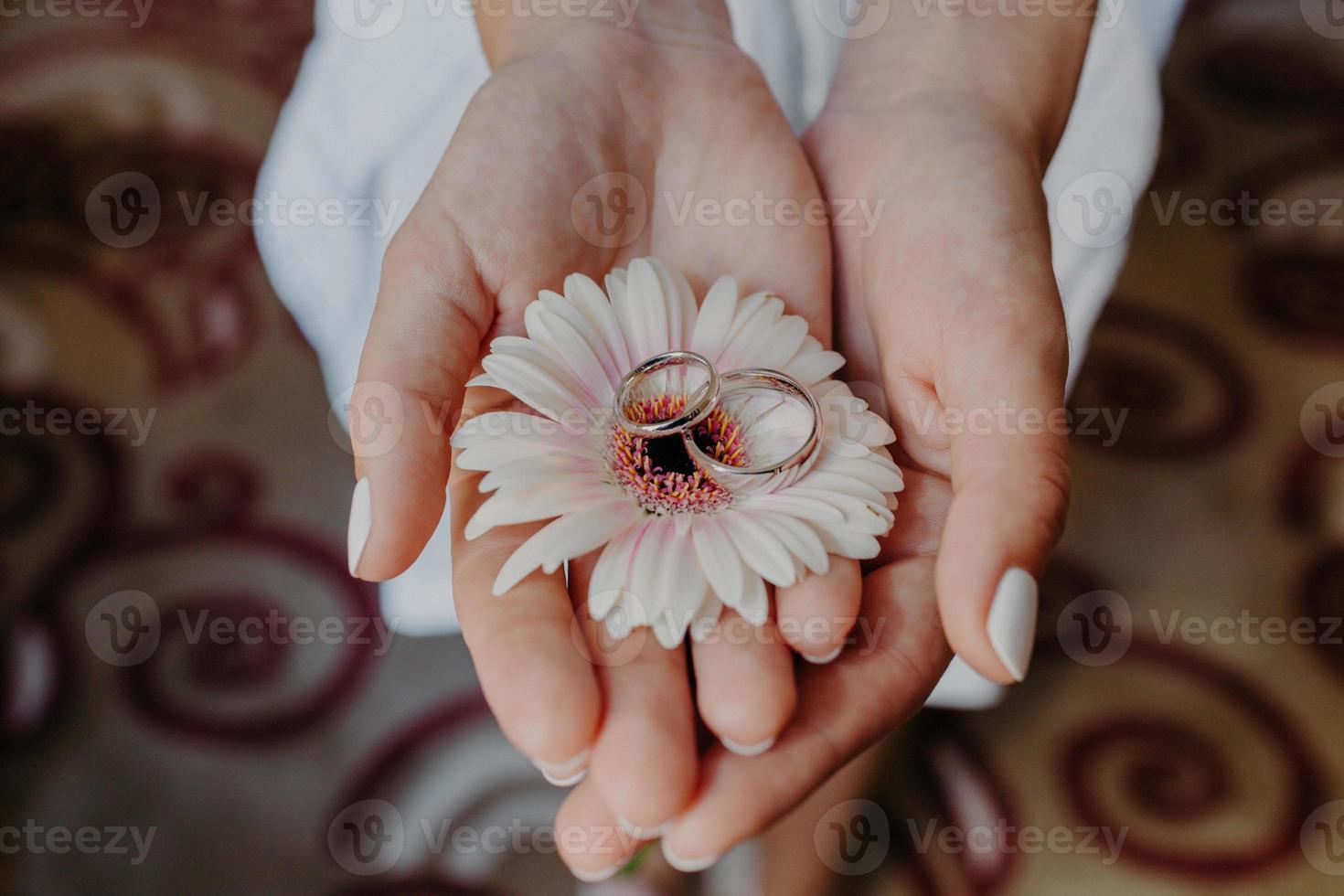 Bridal accessories. Wedding rings on beautiful flower in woman gentle hands indoor. Horizontal shot. Holiday and celebration concept photo