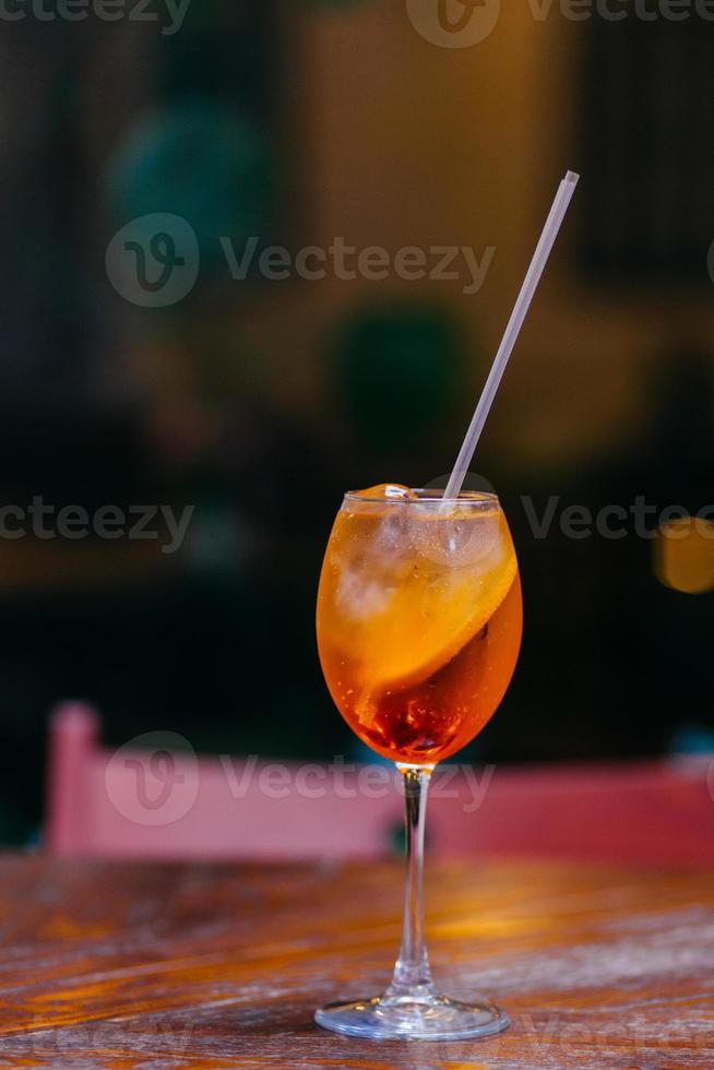 Aperol spiritz cocktail contains alcohol and juice, cold ice and orange, stands in wine glass on wooden table, served in restaurant for visitors photo
