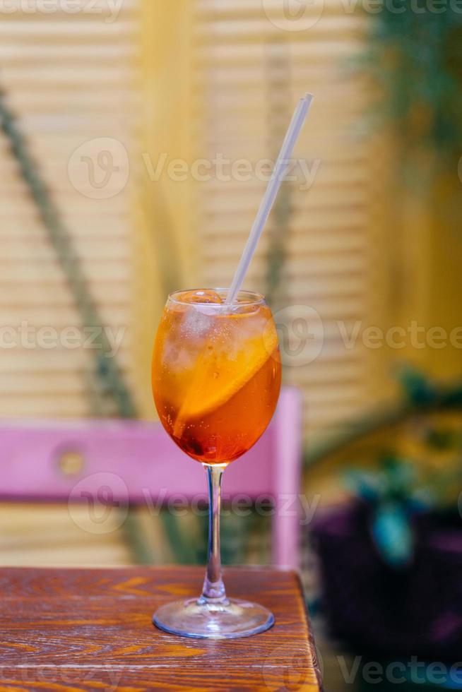 Orange fresh aperol spiritz cocktail on wooden table against blurred background. Summer cold beverage prepared for dinner party. Simple drink with ice and orange photo