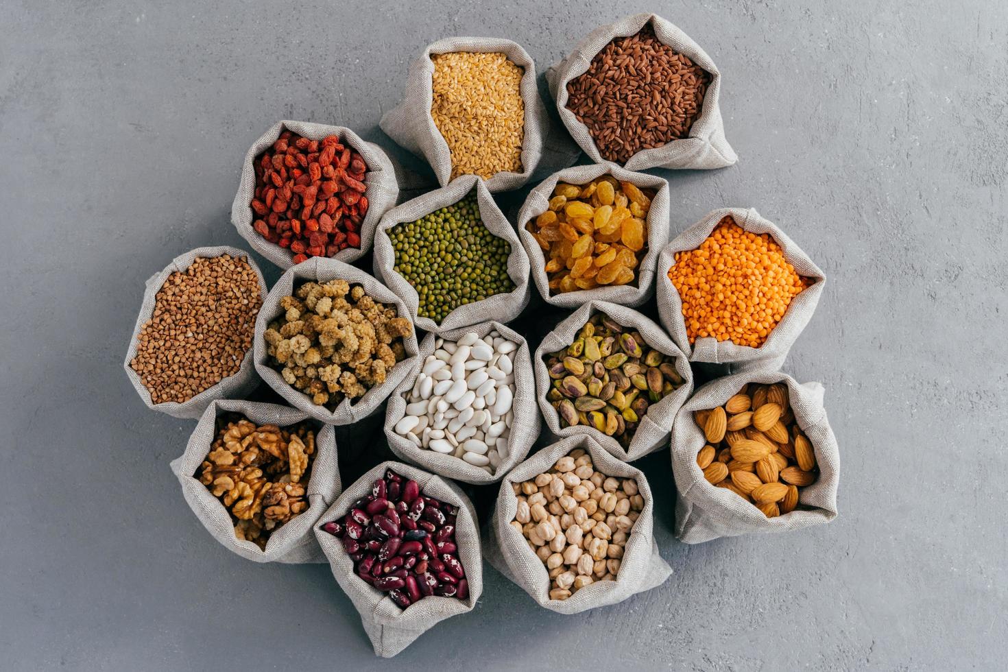 Top view of small bags with cereal grains buckwheat, lentil, haricot, chickpea, goji, raisins, pistache, Chickasano pea, mulberry, sycamin, almond. Collection set photo