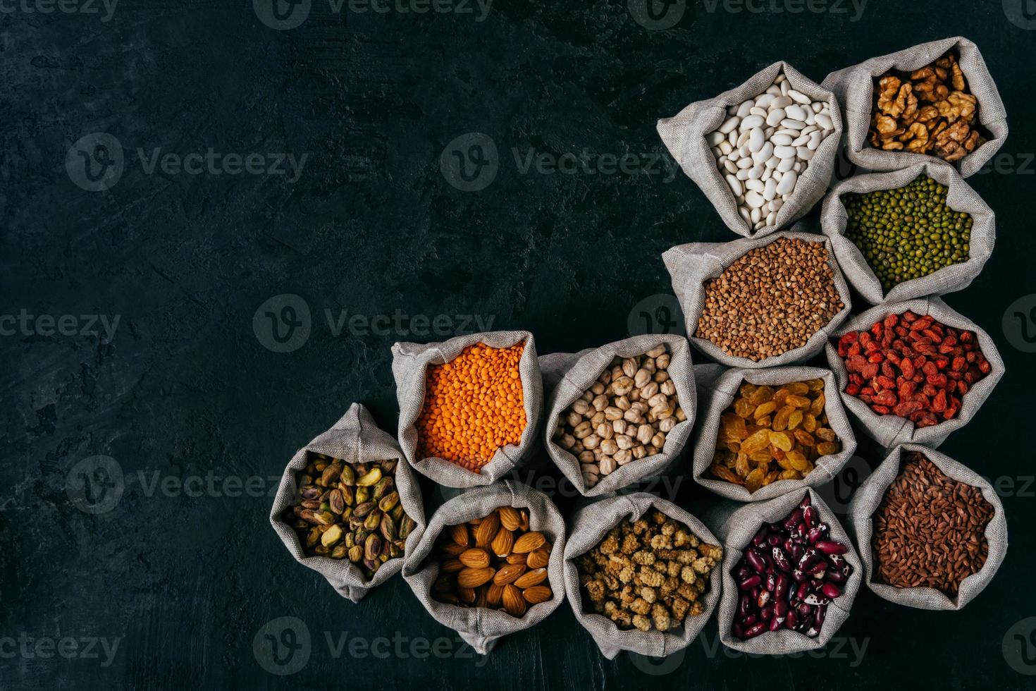 Horizontal shot of little sacks filled with almonds, walnuts, raisins, garbanzo, kidney bean, red goji, isolated over dark background, blank space for your advert photo