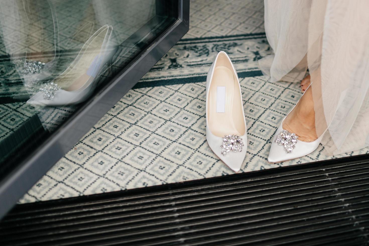 Unrecognizable bride in white dress, puts on wedding shoes, has tender feet, preparares for special occasion in her life. Brides white luxury shoes photo