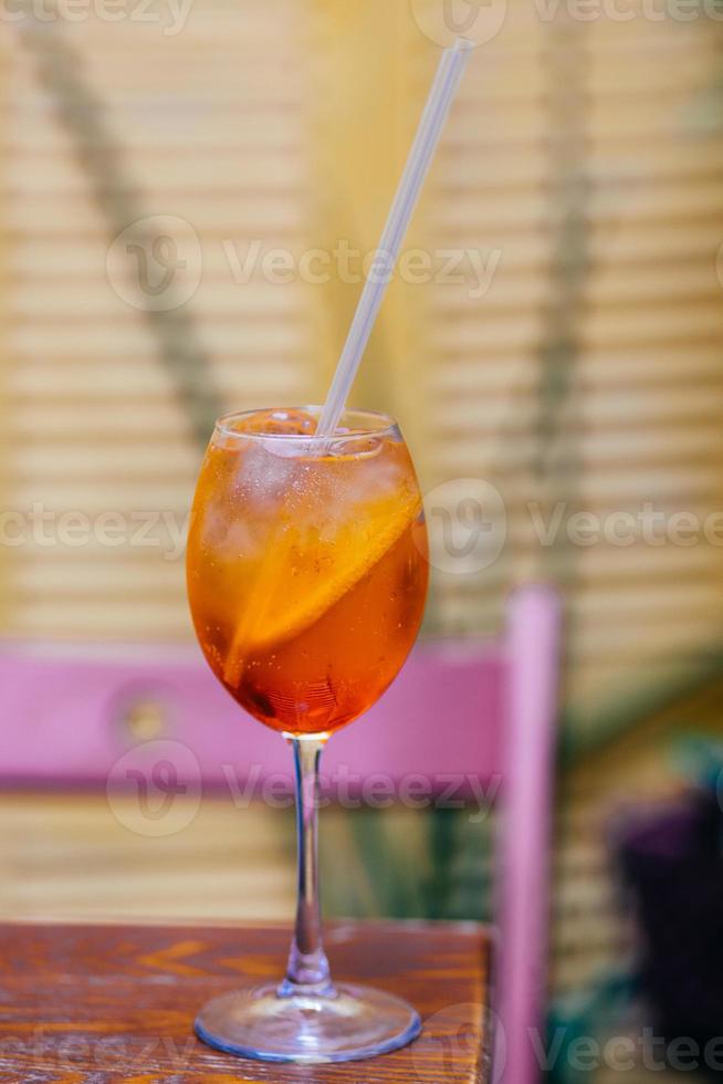 Aperitif cocktail consisting of prosecco, Aperol and soda water, stands in wine glass on wooden table in bar. Aperol spiritz cocktail with several cubes of ice and slice of orange. photo