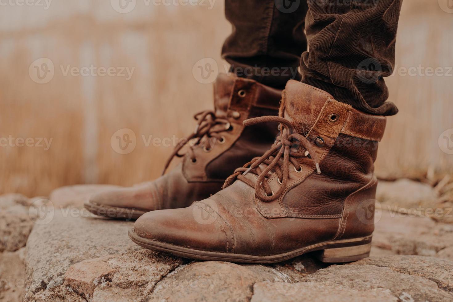 Image of man in brown old leather boots and trousers stands on stones against blurred background. Shabby shoes. Selling of shoes. Coming winter photo