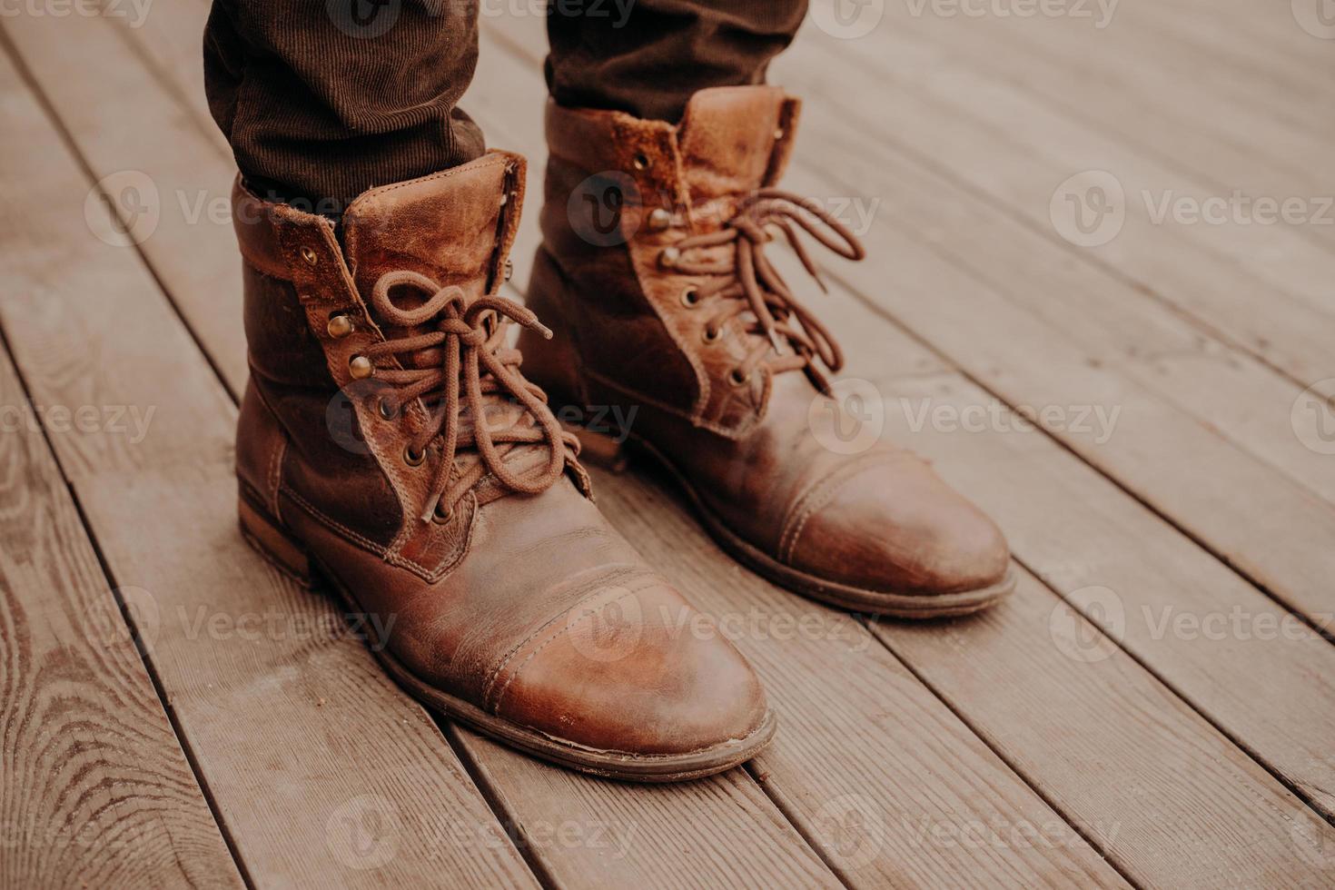 Top view of mans shoes on wooden floor or surface. Old footwear. Unrecognizable man. Leather shaggy brown boots with laces photo