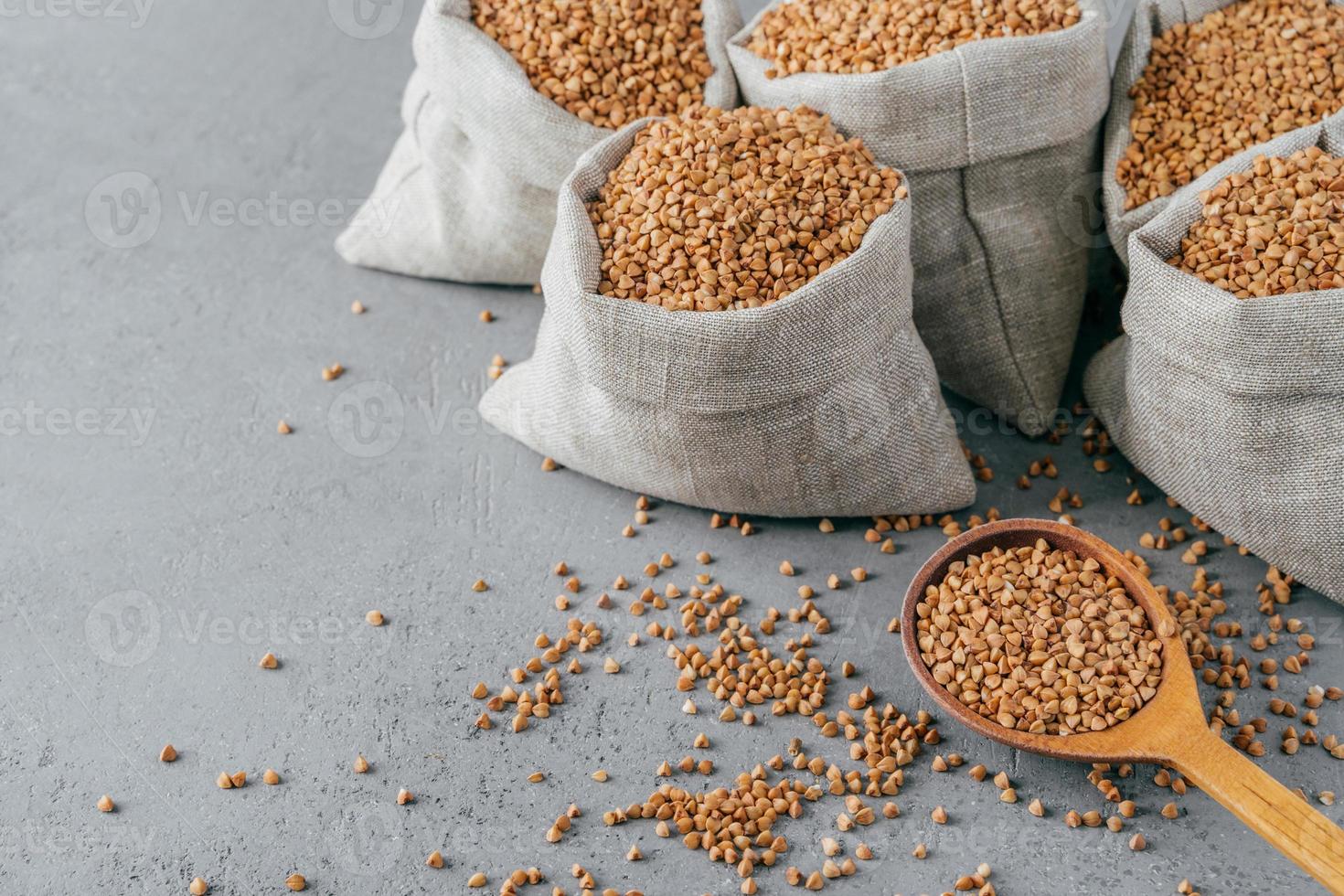 Eco food and clean eating concept. Buckwheat in small linen bags. Wooden spoon filled with protein product, Copy space on grey background. photo