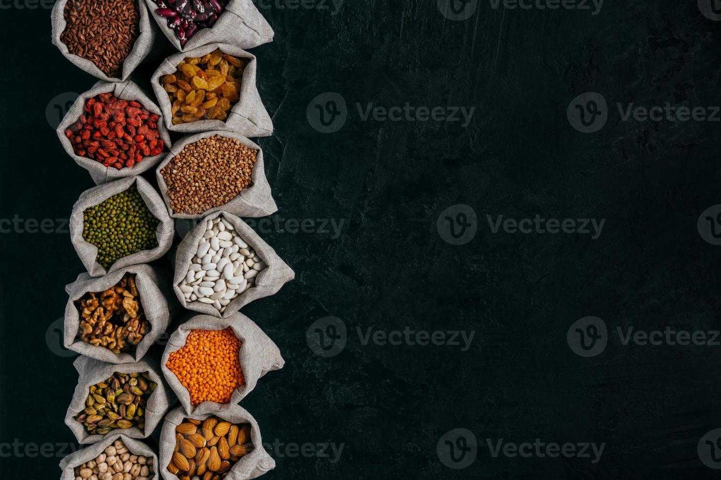 Photo of healthy food ingredients in little sacks, isolated over black background with empty space for your promotion. Bags of cereals and beans, fruit in one row