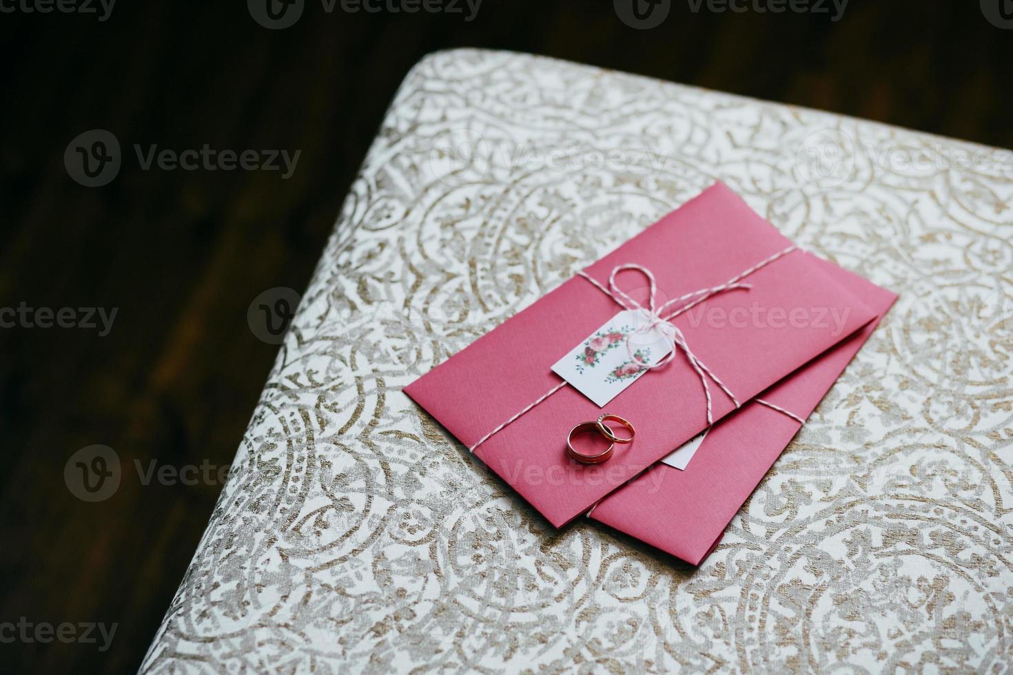 Wedding rings lying on pink invitation card. Wedding preparations and decorations. Wedding card made by groom and bride. Love and romance concept photo