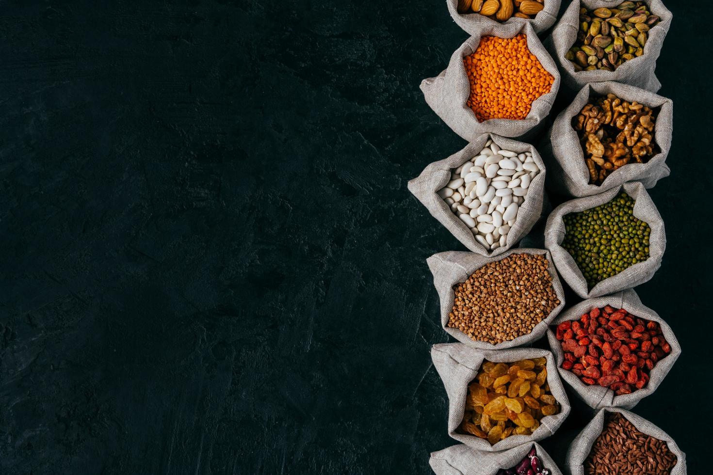 Top view of little sacks filled with bean seeds and dried fruit, isolated over black background with copy space for your advertisement photo