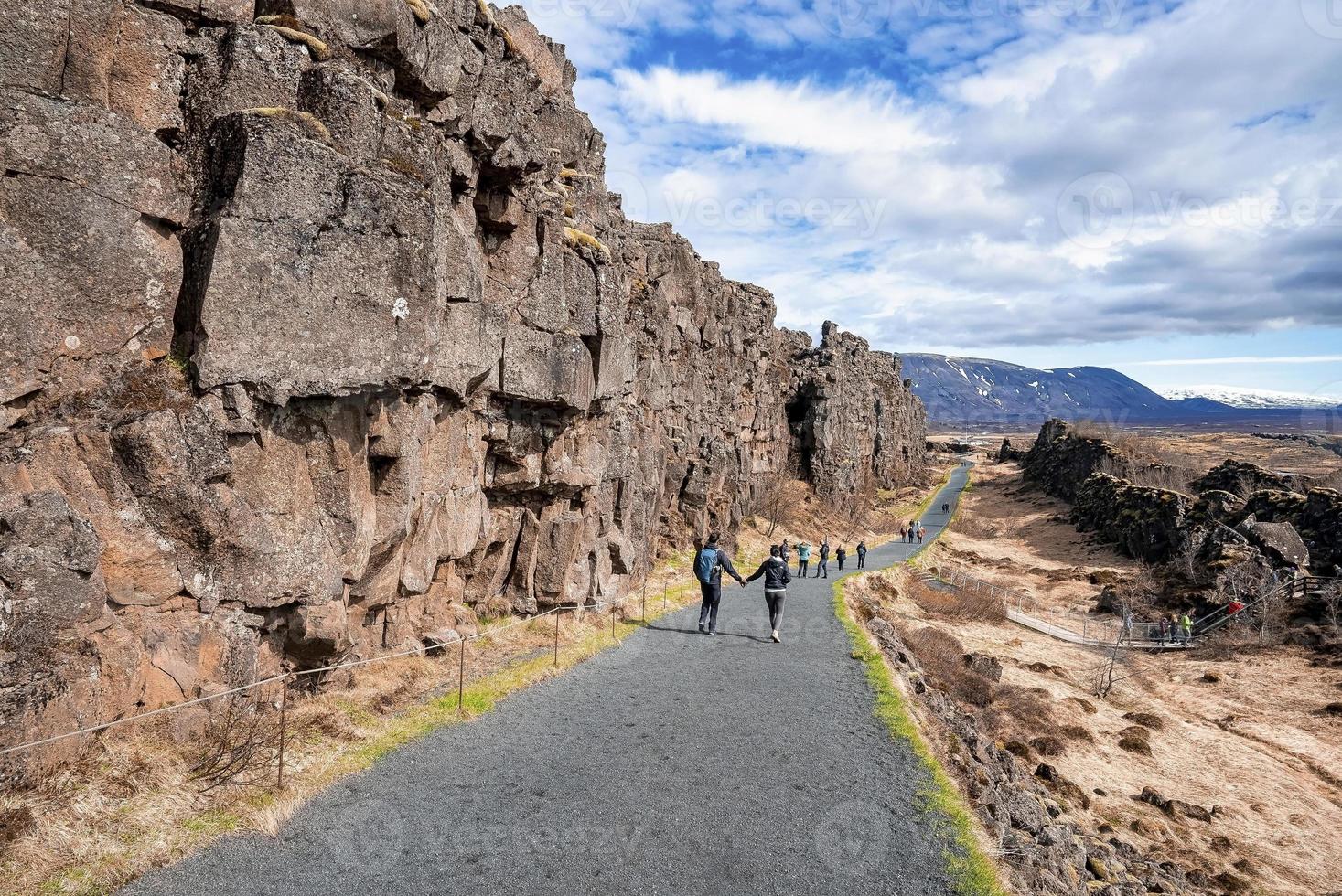 turistas caminando por la carretera por acantilados contra el cielo azul en el parque nacional de Thingvellir foto