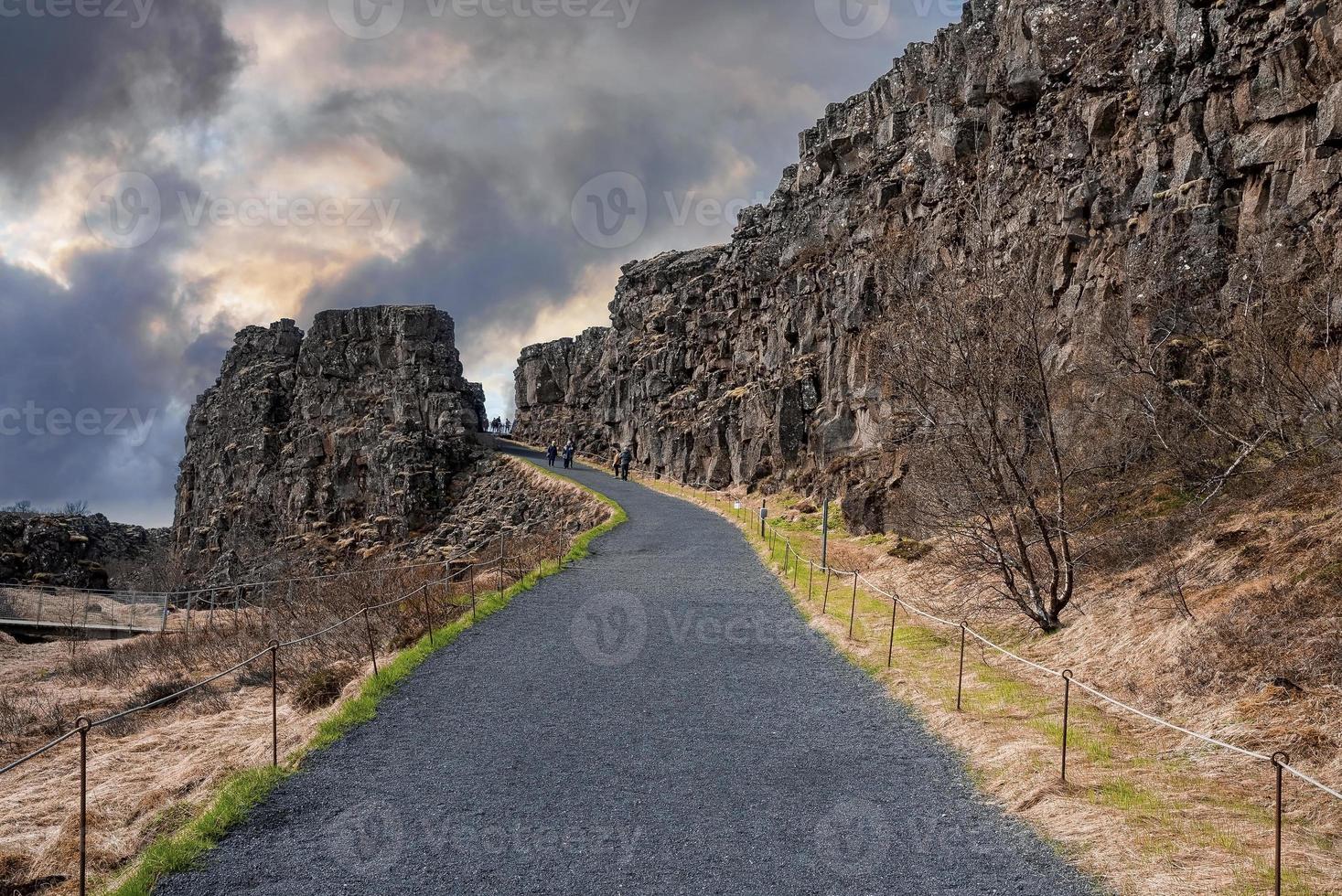People walking on road by cliffs against cloudy sky at Thingvellir national park photo