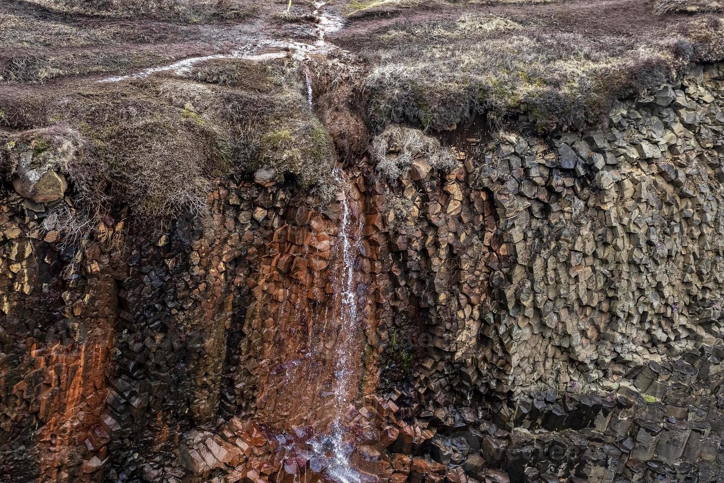 View of small waterfall falling over basalt rock columns on cliff in valley photo